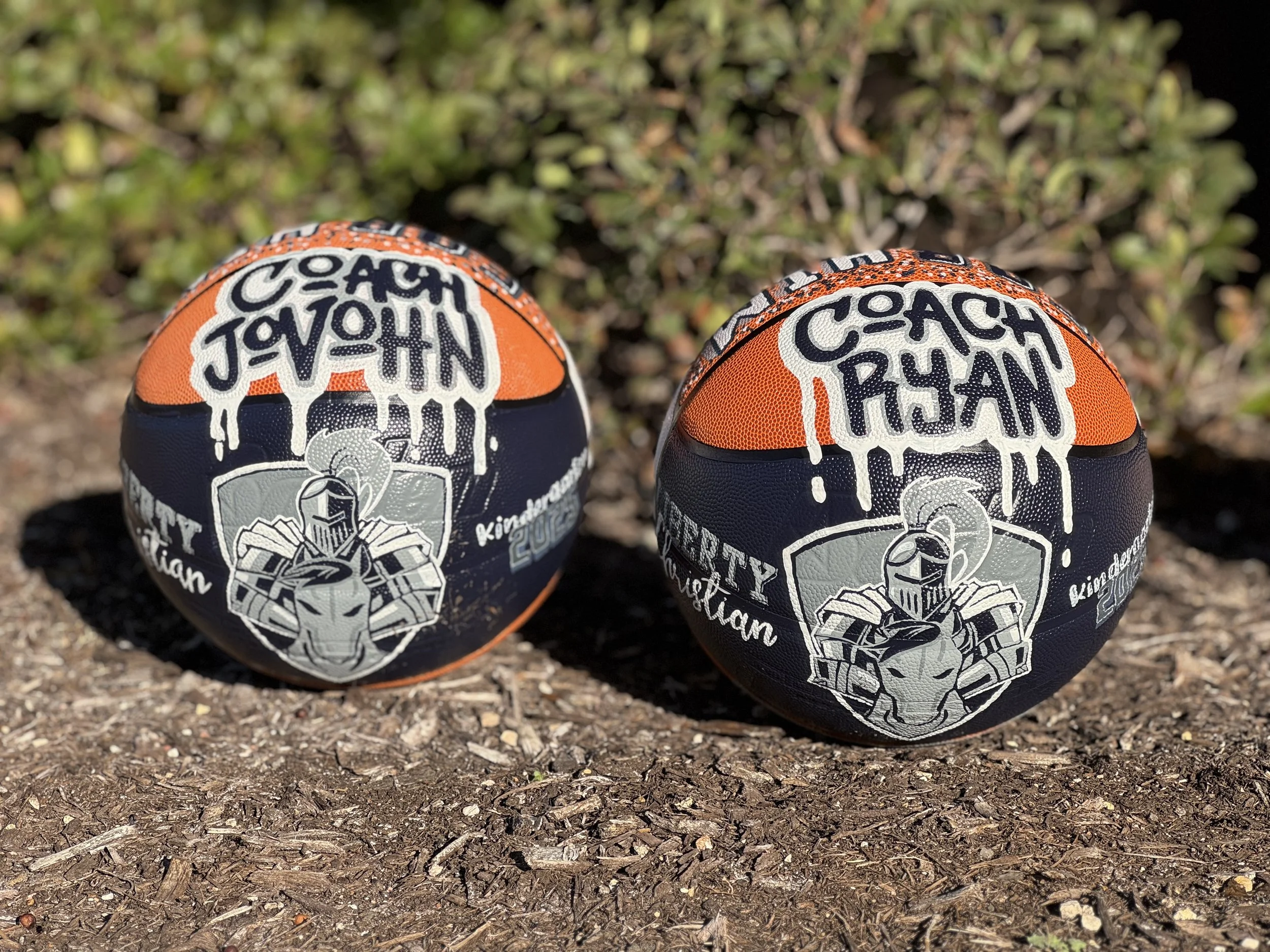Two hand-painted basketballs personalized for coaches with team colors and mascot artwork