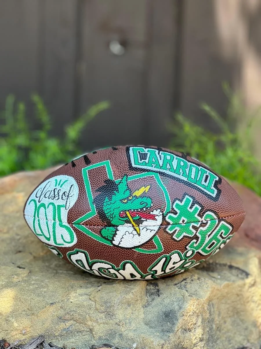 Custom football with Carroll Dragon mascot within the outline of the state of Texas, resting on a rock.