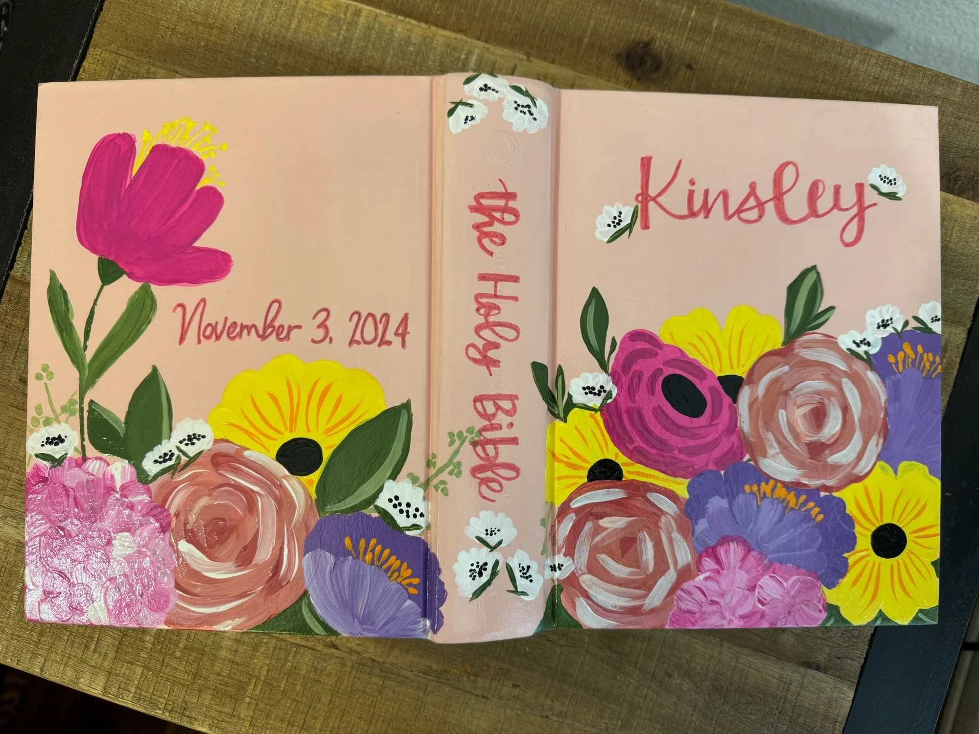 Personalized hand-painted Bible for Kinsley featuring bright pink, yellow and purple flowers, her name and birth date.