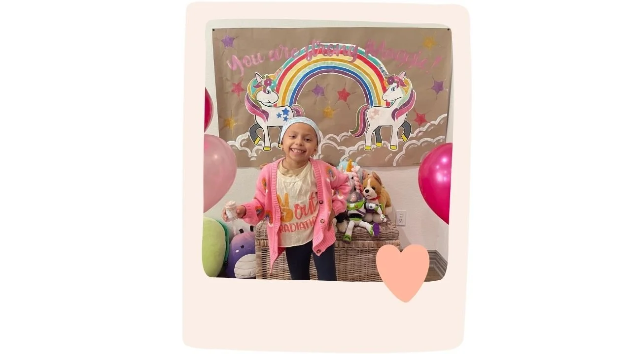 Young girl named Maggie smiling in front of a custom-painted banner featuring colorful unicorns, rainbows, and stars, with balloons and plush toys surrounding her.