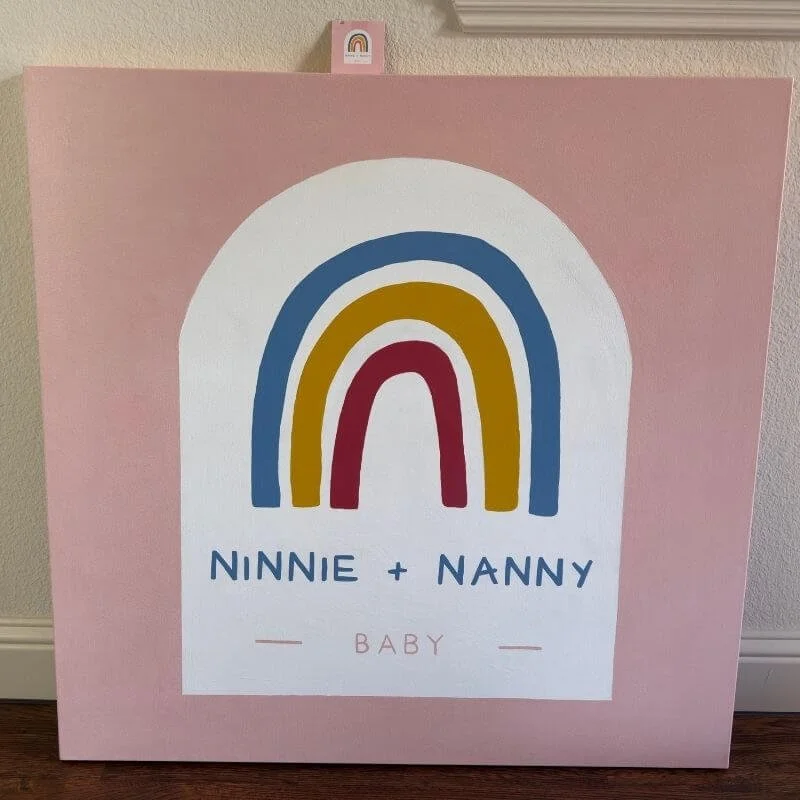Pink canvas with a white arch featuring a colorful rainbow and text "Ninnie + Nanny Baby."