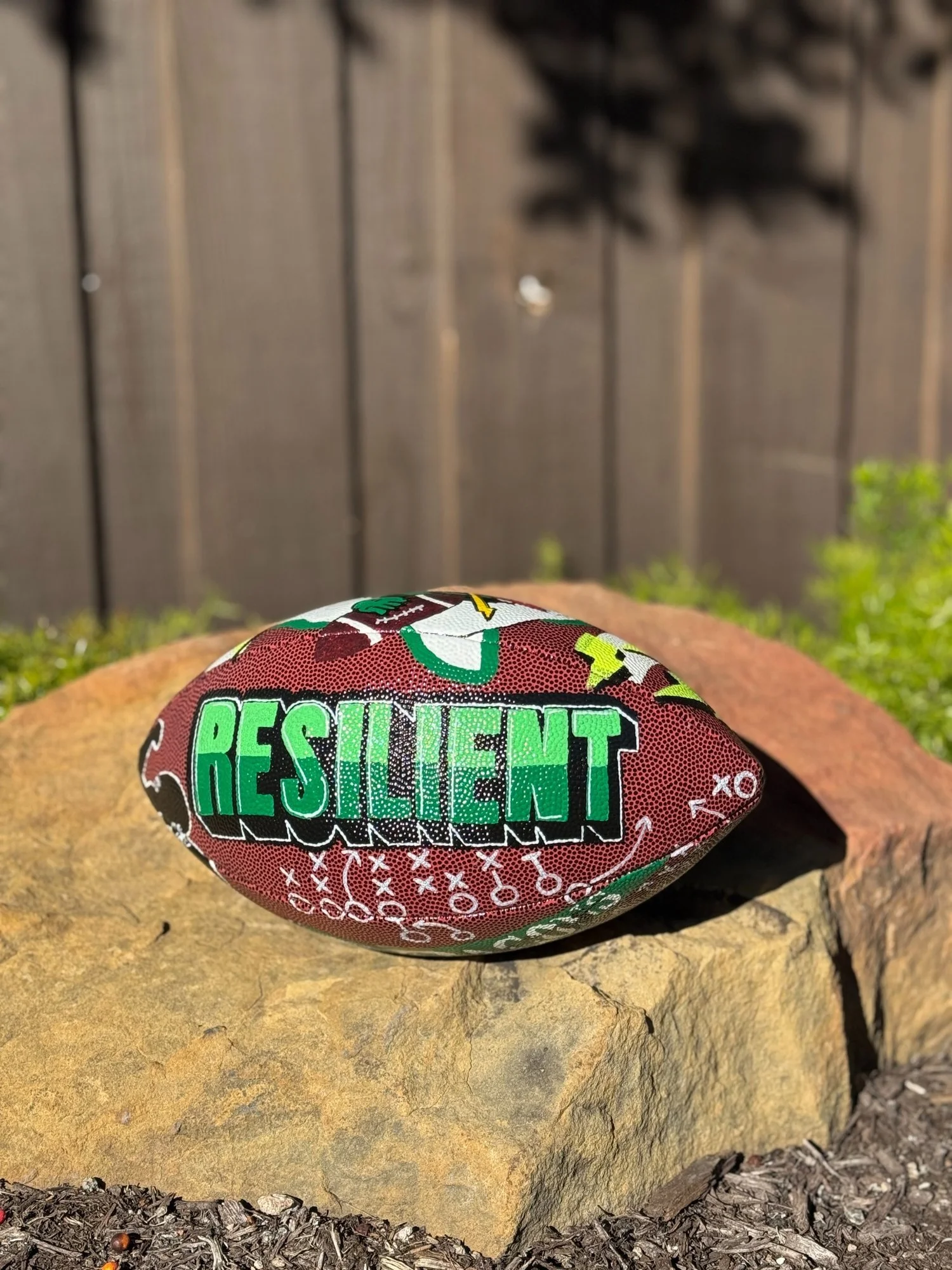 Hand-painted personalized football featuring the word Resilient, created to celebrate an athlete's comeback after a serious injury