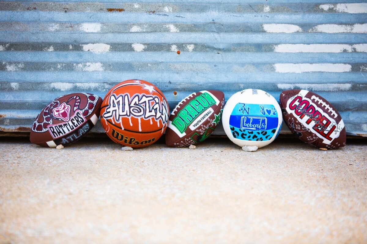 Collection of hand-painted sports balls, including footballs and a basketball, placed against a rustic background.