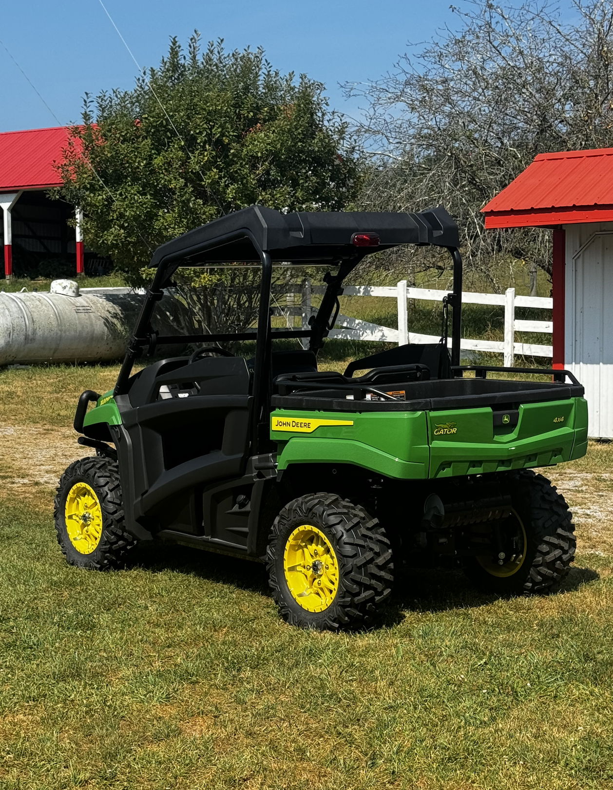 Green John Deere Gator utility vehicle with yellow wheels parked on grass near farm buildings.