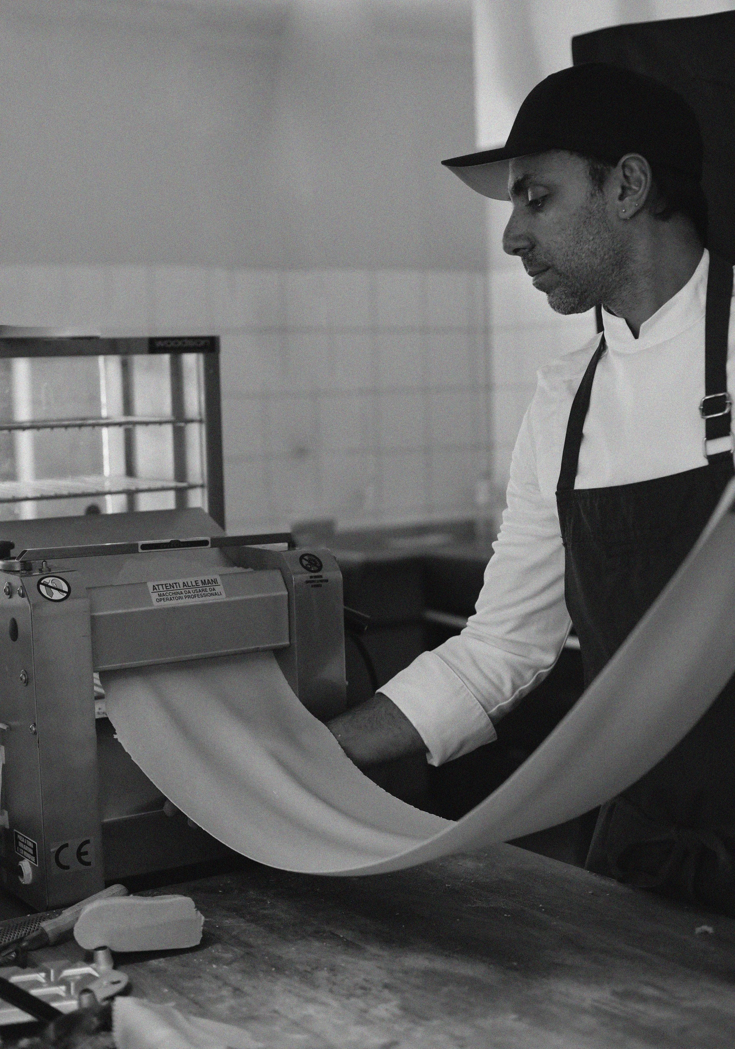 Chef using pasta machine rolling dough in kitchen.