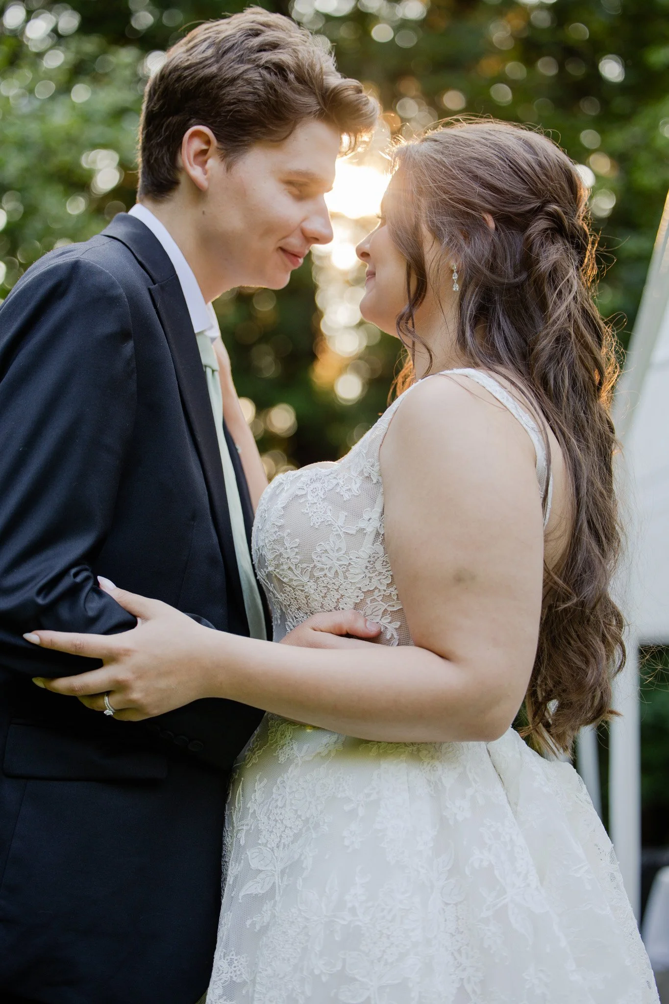 A bride and groom share a close moment during their wedding, standing outdoors with the setting sun behind them.