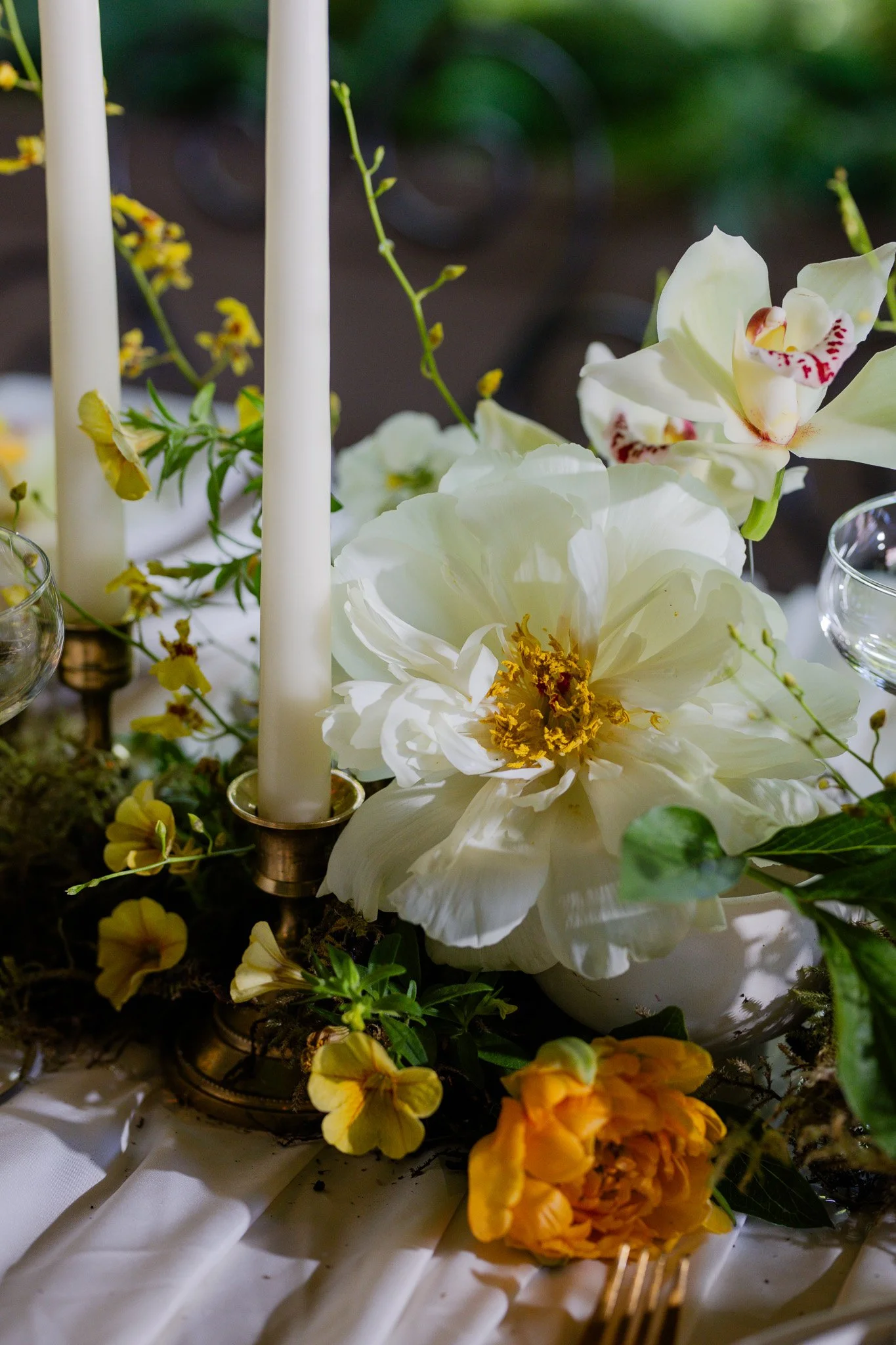 Close-up of a table setting with white and yellow flowers and candles, likely for a celebration or event.