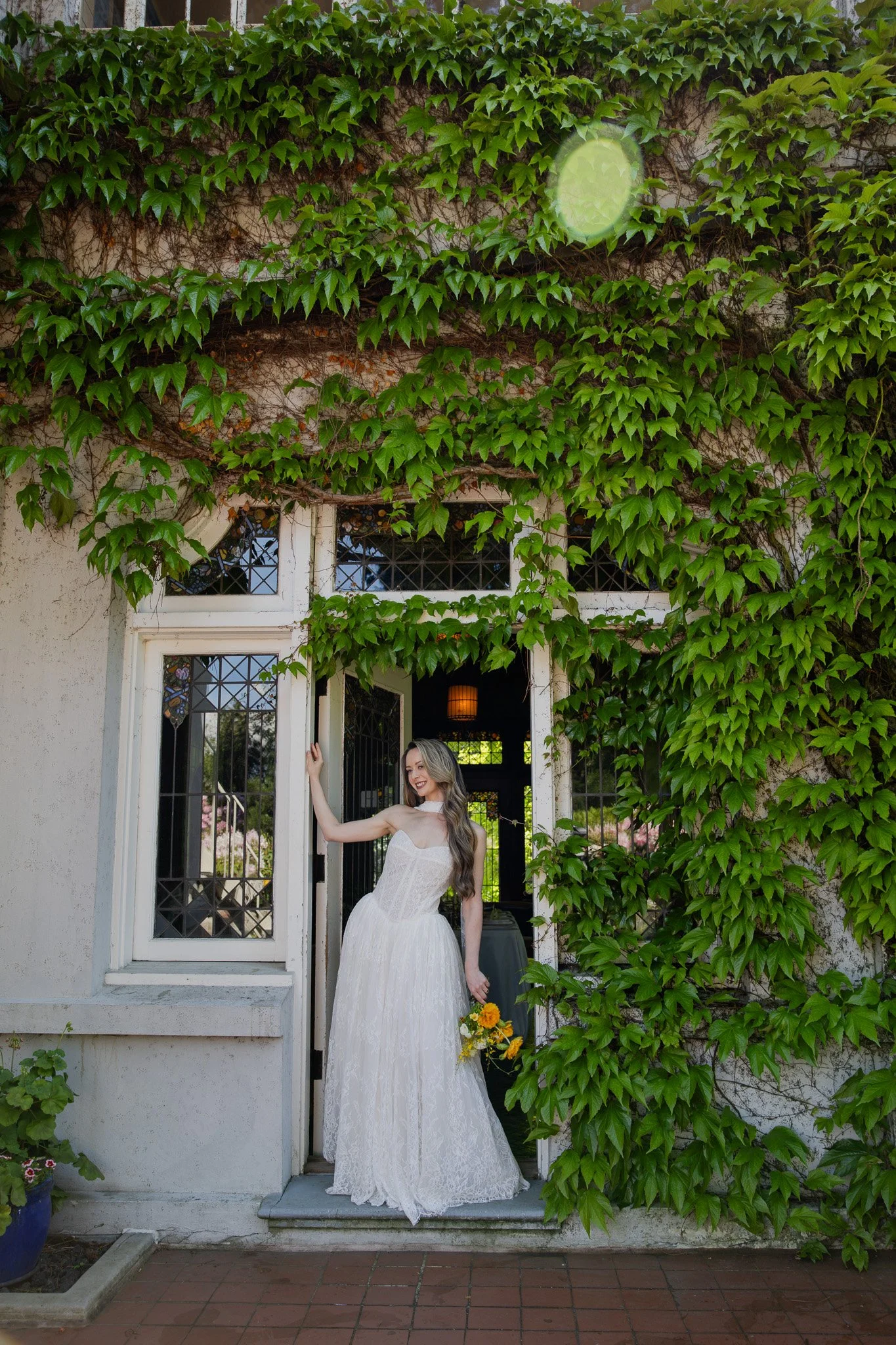 A bride wearing a white dress holding a bouquet of white flowers including roses and lisianthus, with a diamond engagement ring on her finger.