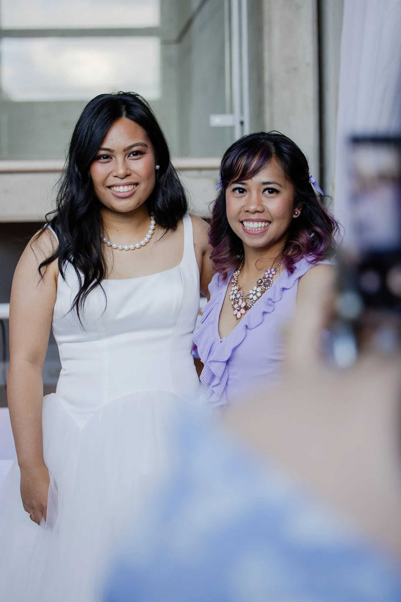 Two women dressed in formal attire smiling and taking a selfie.