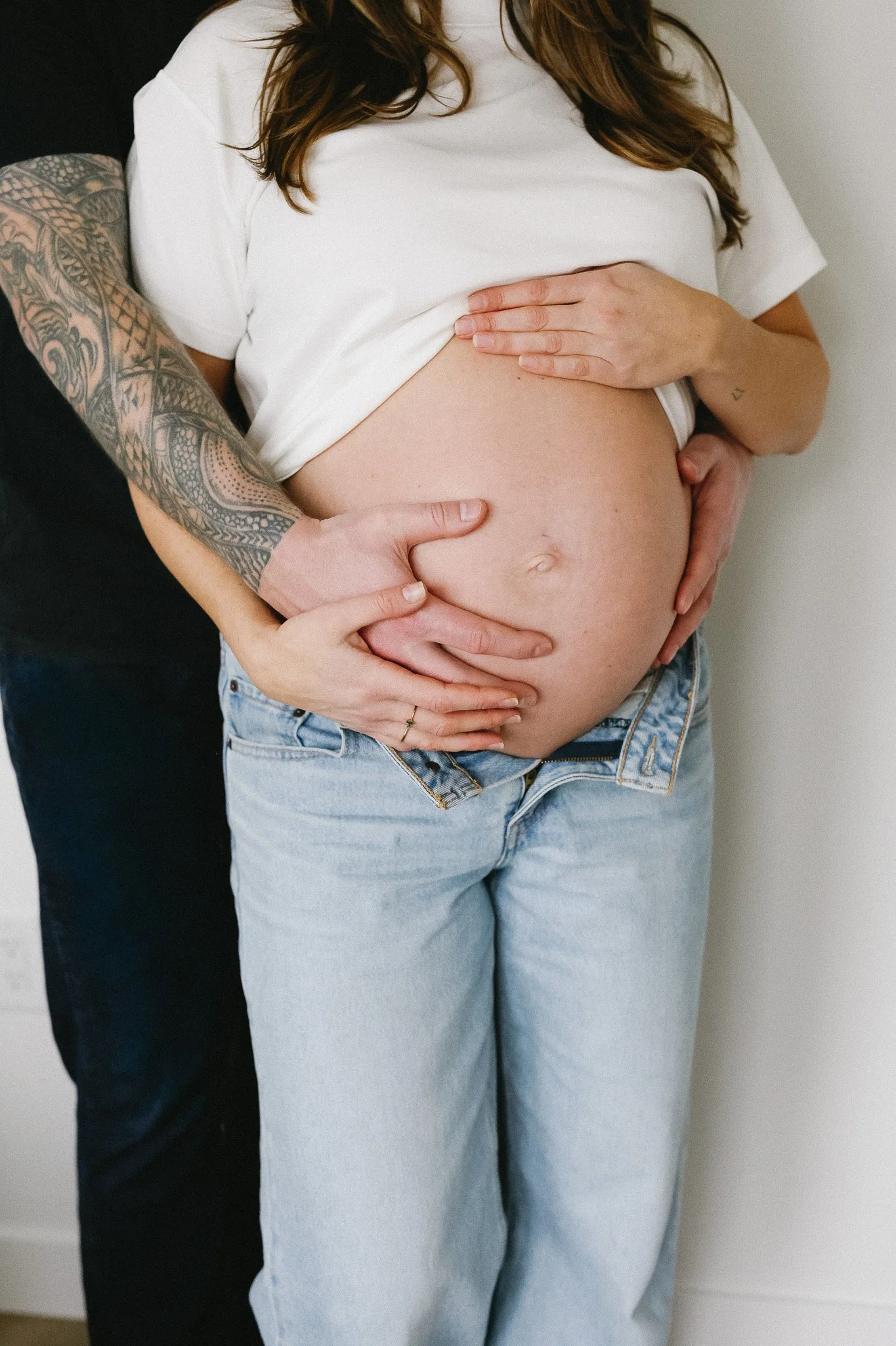A pregnant woman showing her belly, with a man’s hand on her abdomen and her hand resting on top, both gently holding her belly.