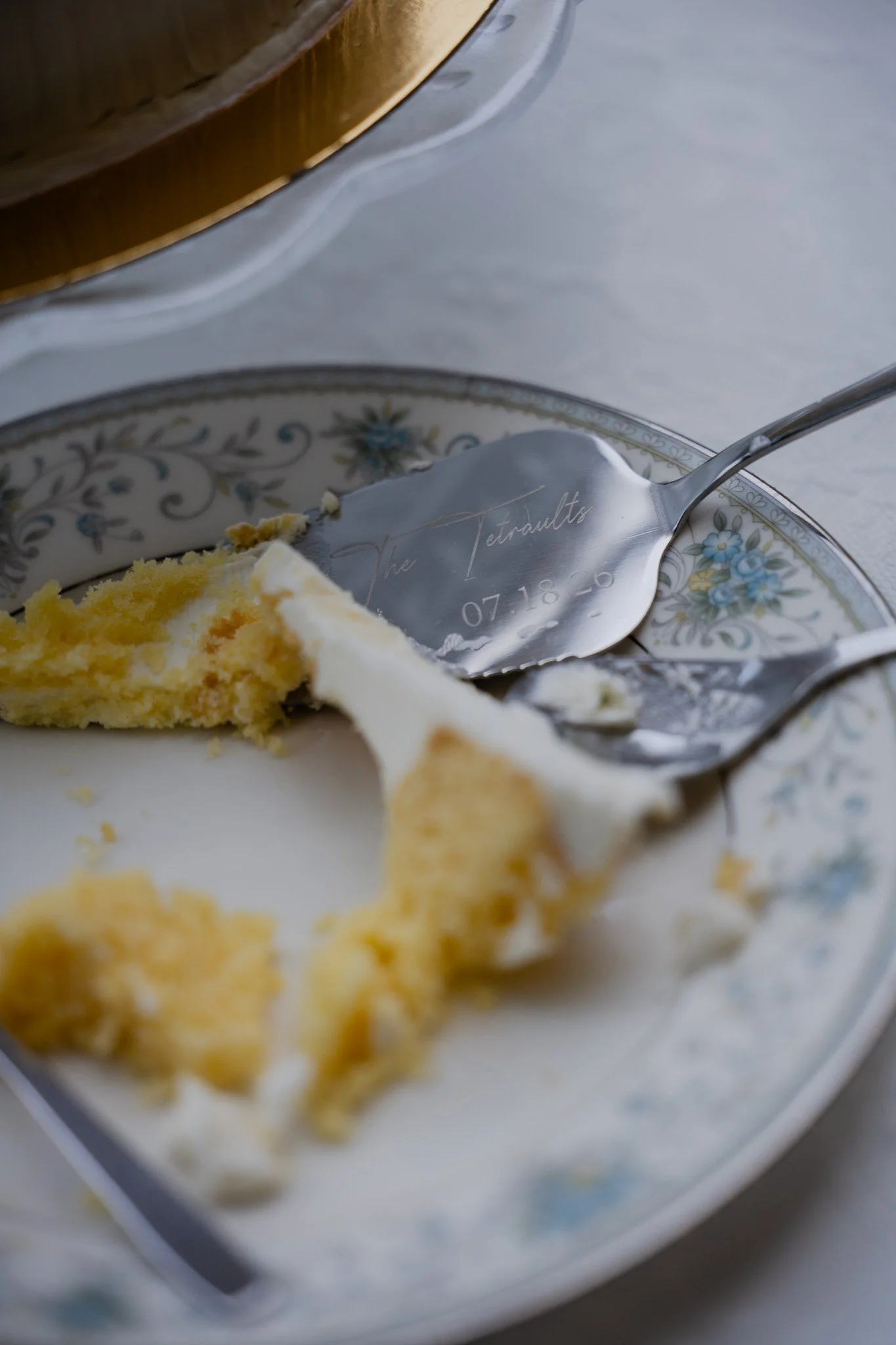 A partially eaten slice of cake on a decorative plate with a spoon inscribed with a name and date, on a white surface.