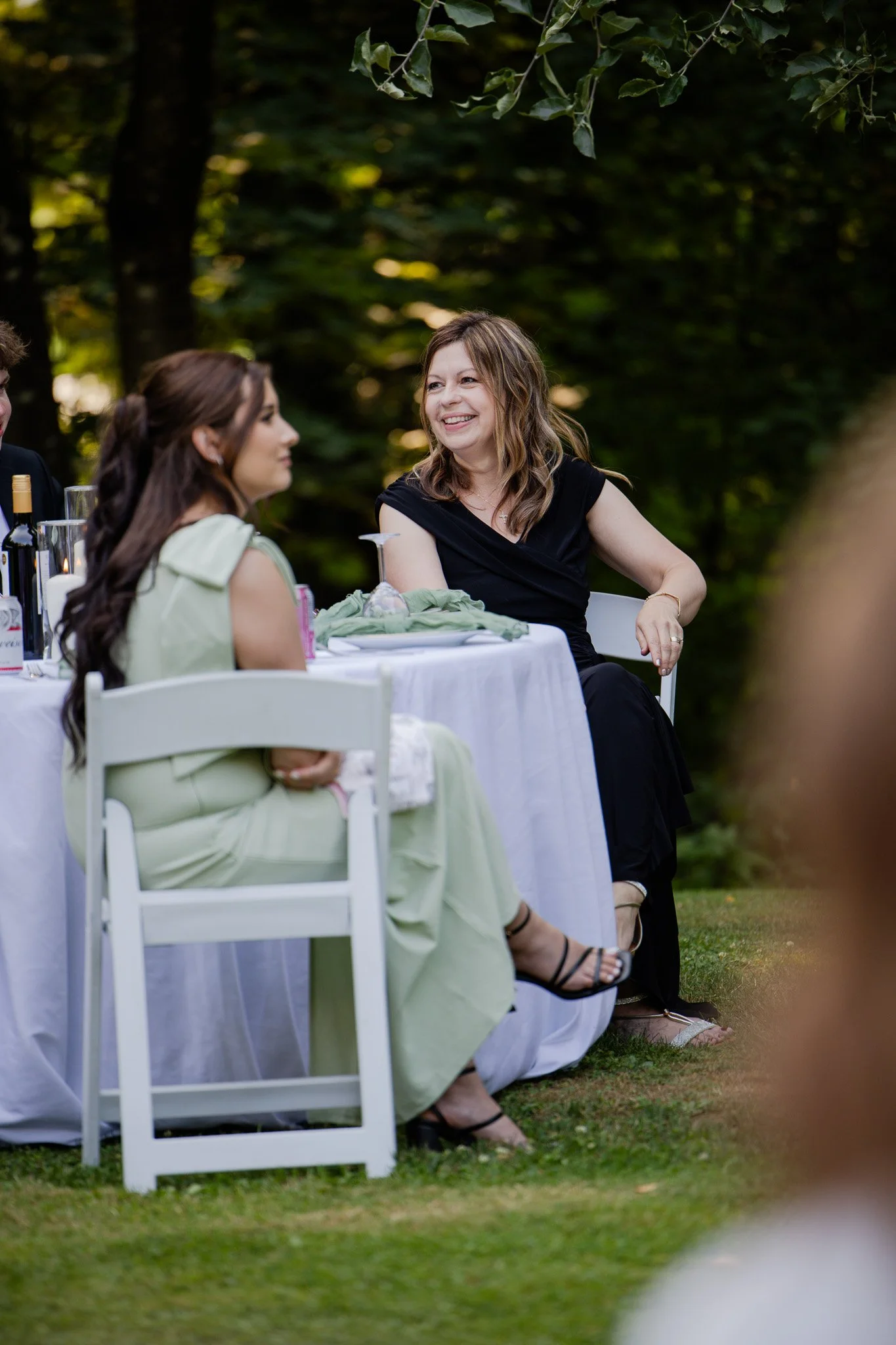 Women sitting at a beautifully decorated outdoor table during daylight, surrounded by trees, enjoying a social gathering or celebration.