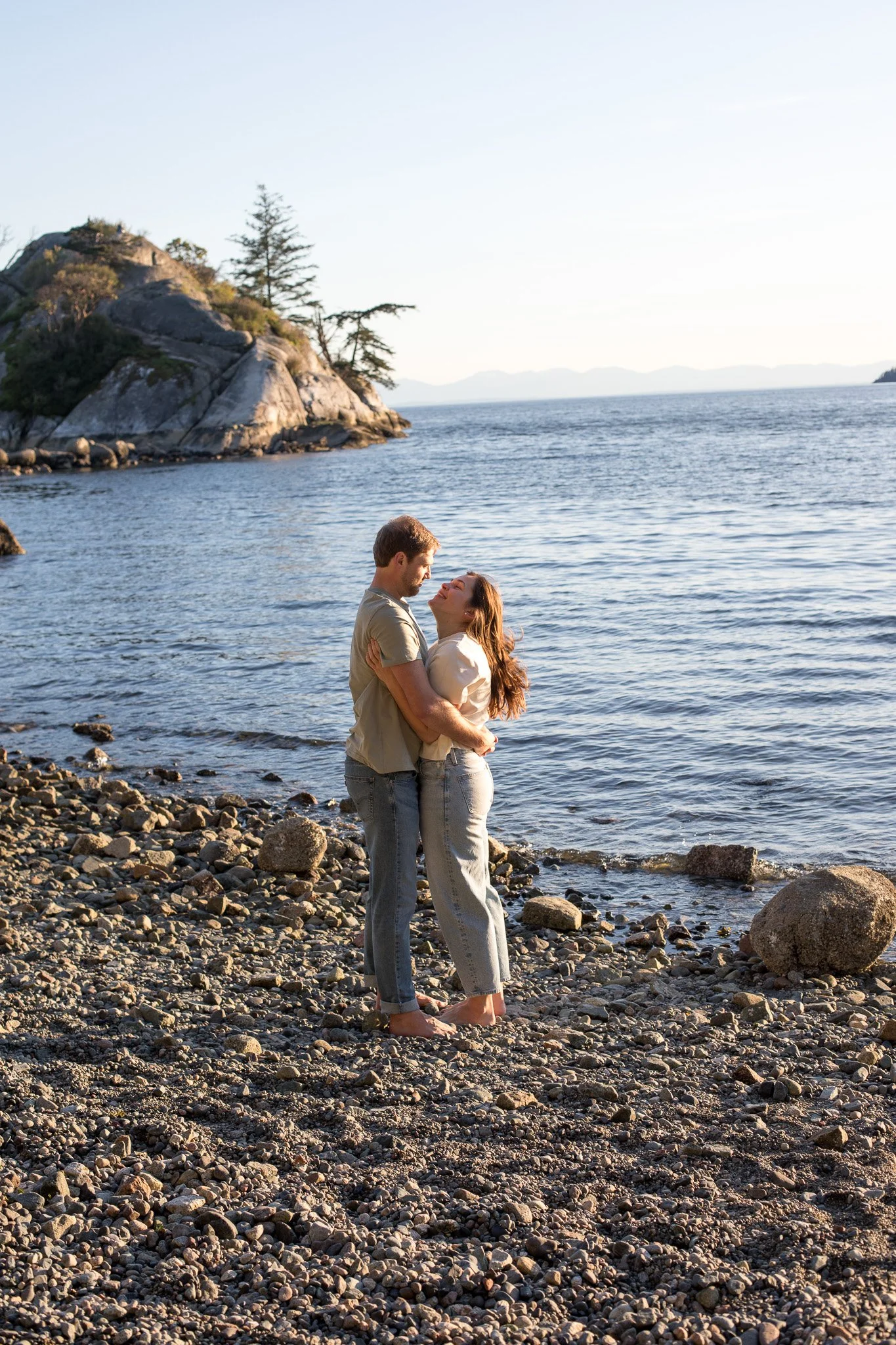 A couple hugging on a rocky beach by the water during sunset.