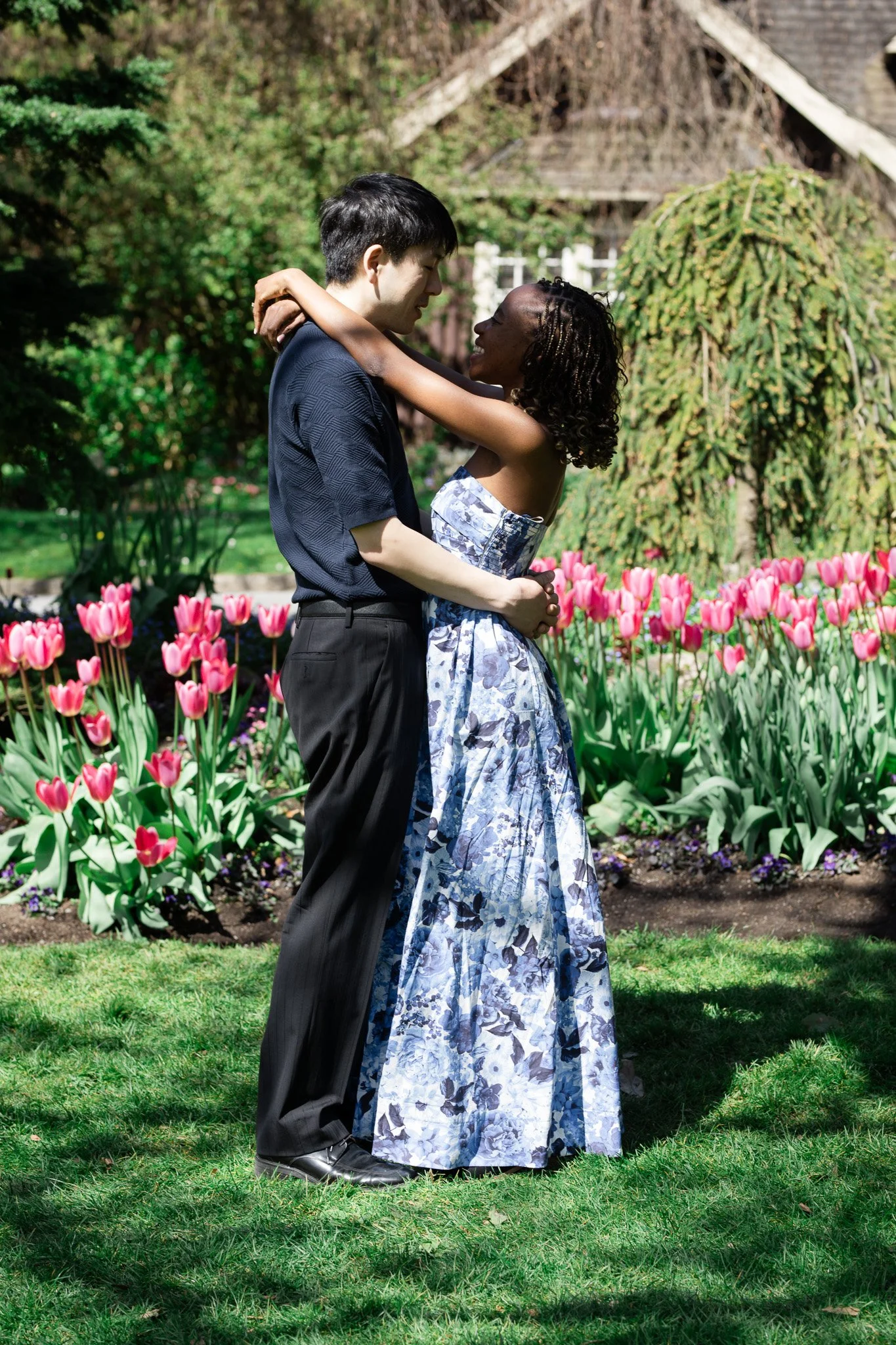 A couple hugging in a garden with pink tulips and green trees.