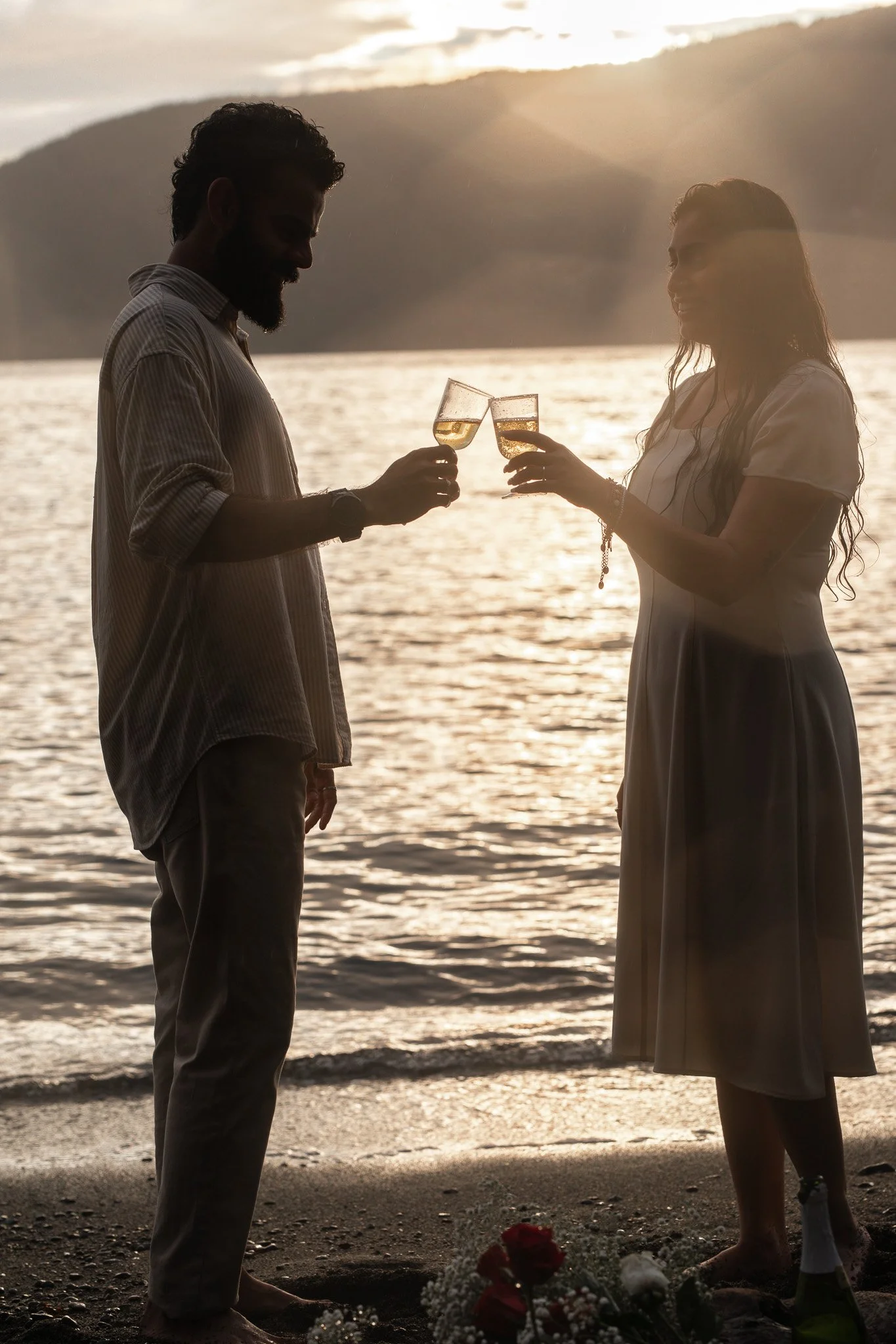 A couple celebrating with champagne glasses at the beach during sunset.