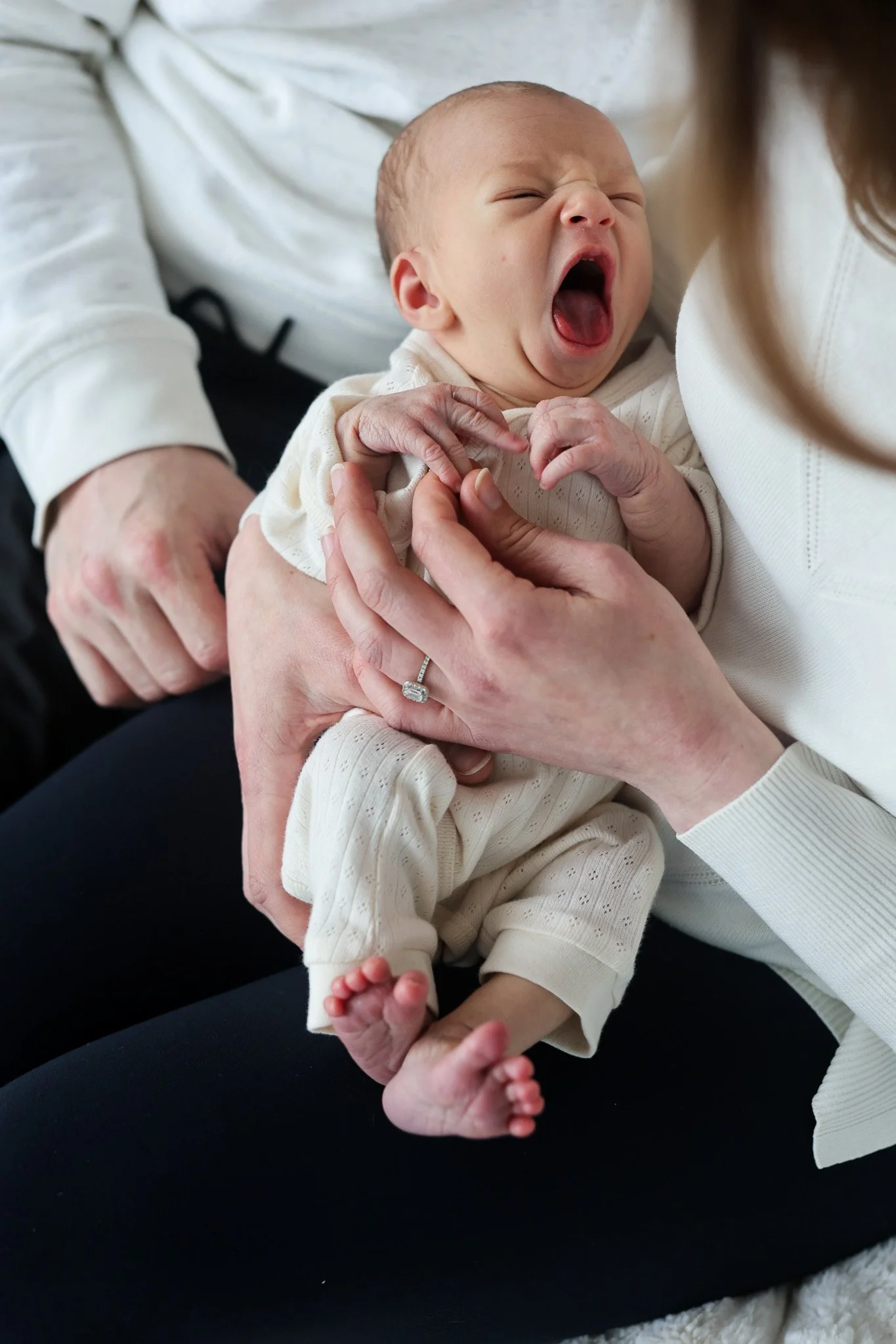 A baby yawning while being held by a person wearing a white top.