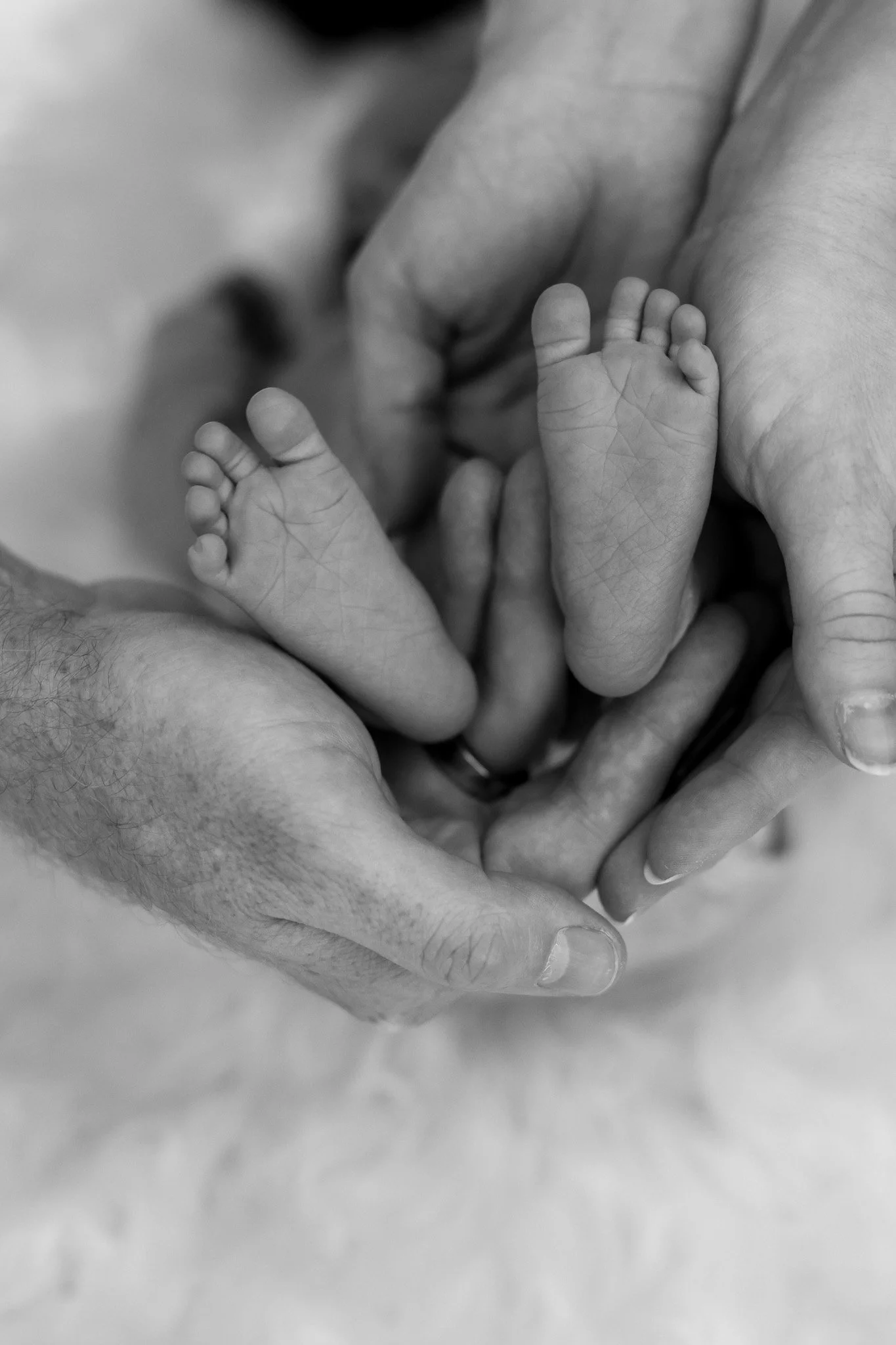 Close-up of a baby's tiny foot being held by an adult's hand in black and white.