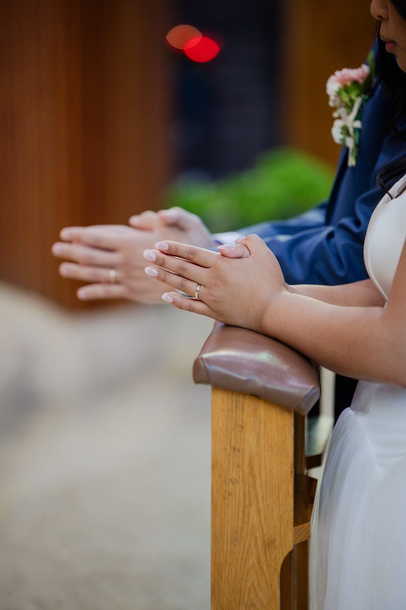 People praying with hands folded on a wooden pew during a religious service.