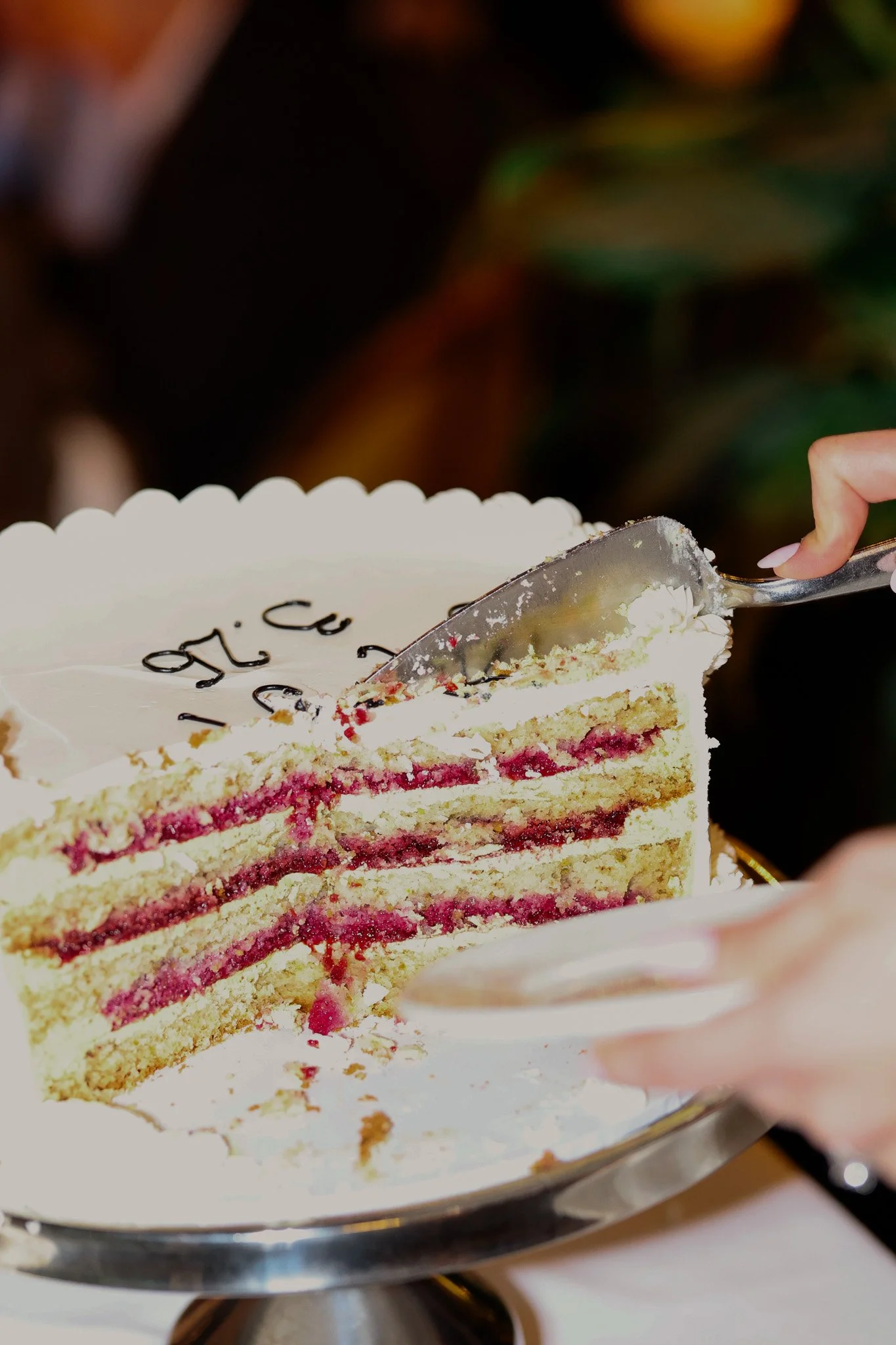 A slice of white layered cake with pink filling, topped with white icing and decorative details, being served with a cake server.
