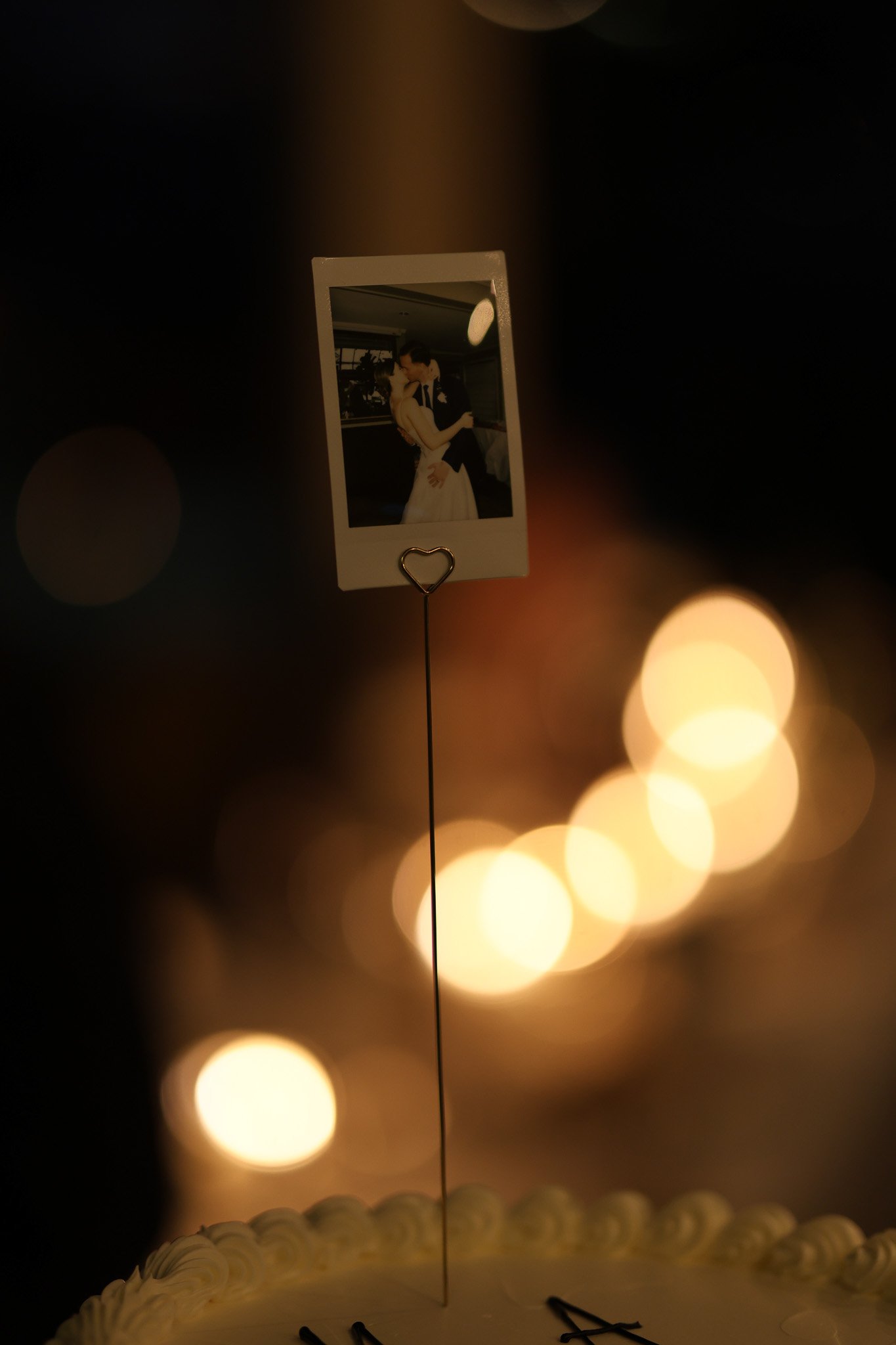A wedding cake with a photograph of a bride and groom on top, illuminated with warm lights.