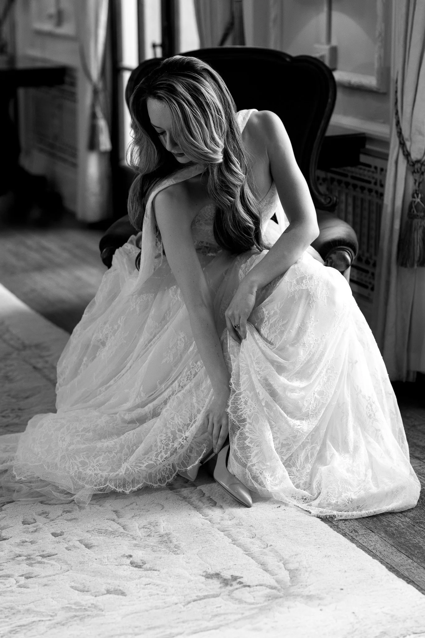 A woman in a wedding dress sitting on a chair, looking down, in black and white.