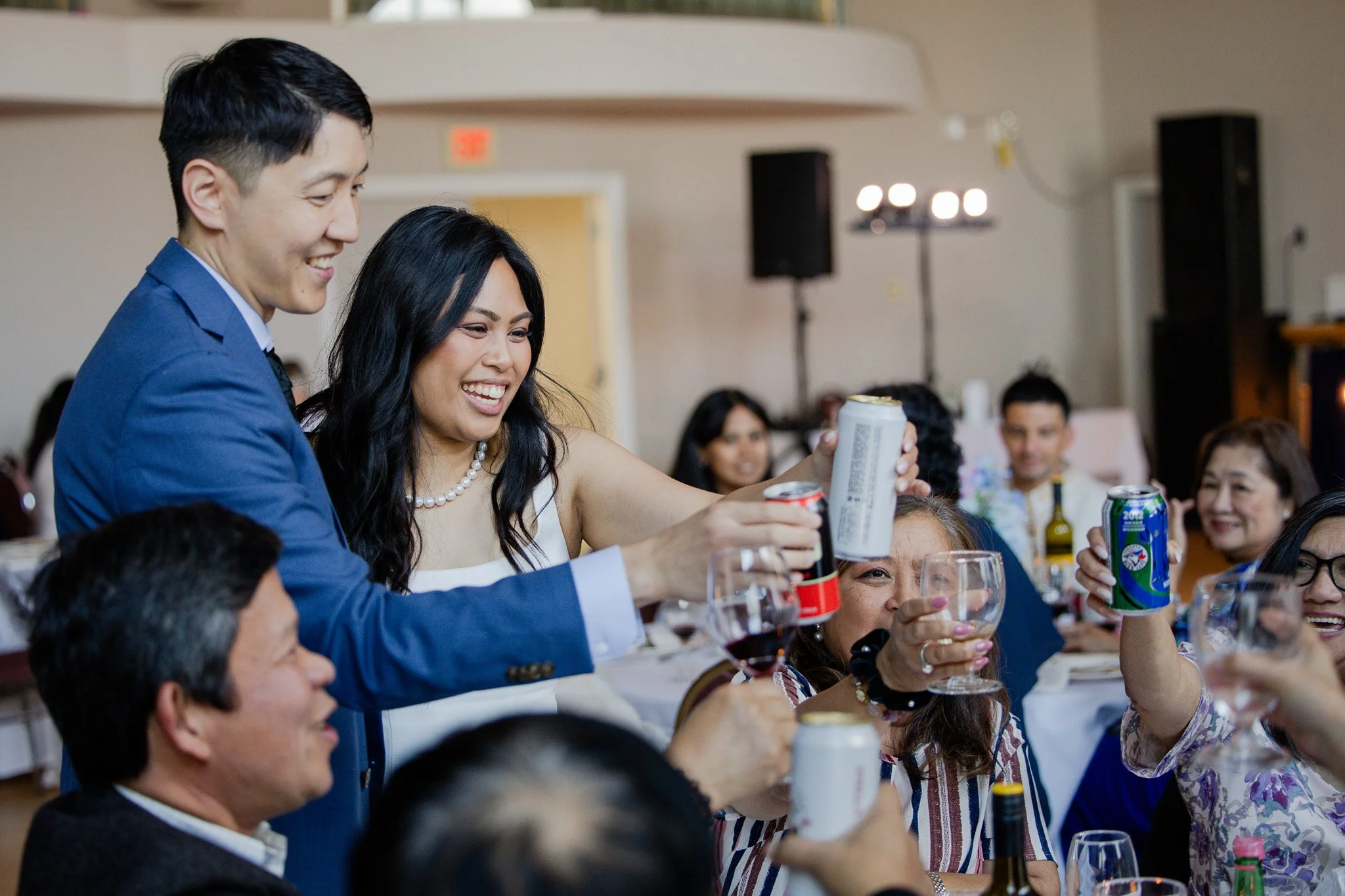 People at a social gathering holding and toasting with canned and bottled beverages, smiling and engaging in conversation.