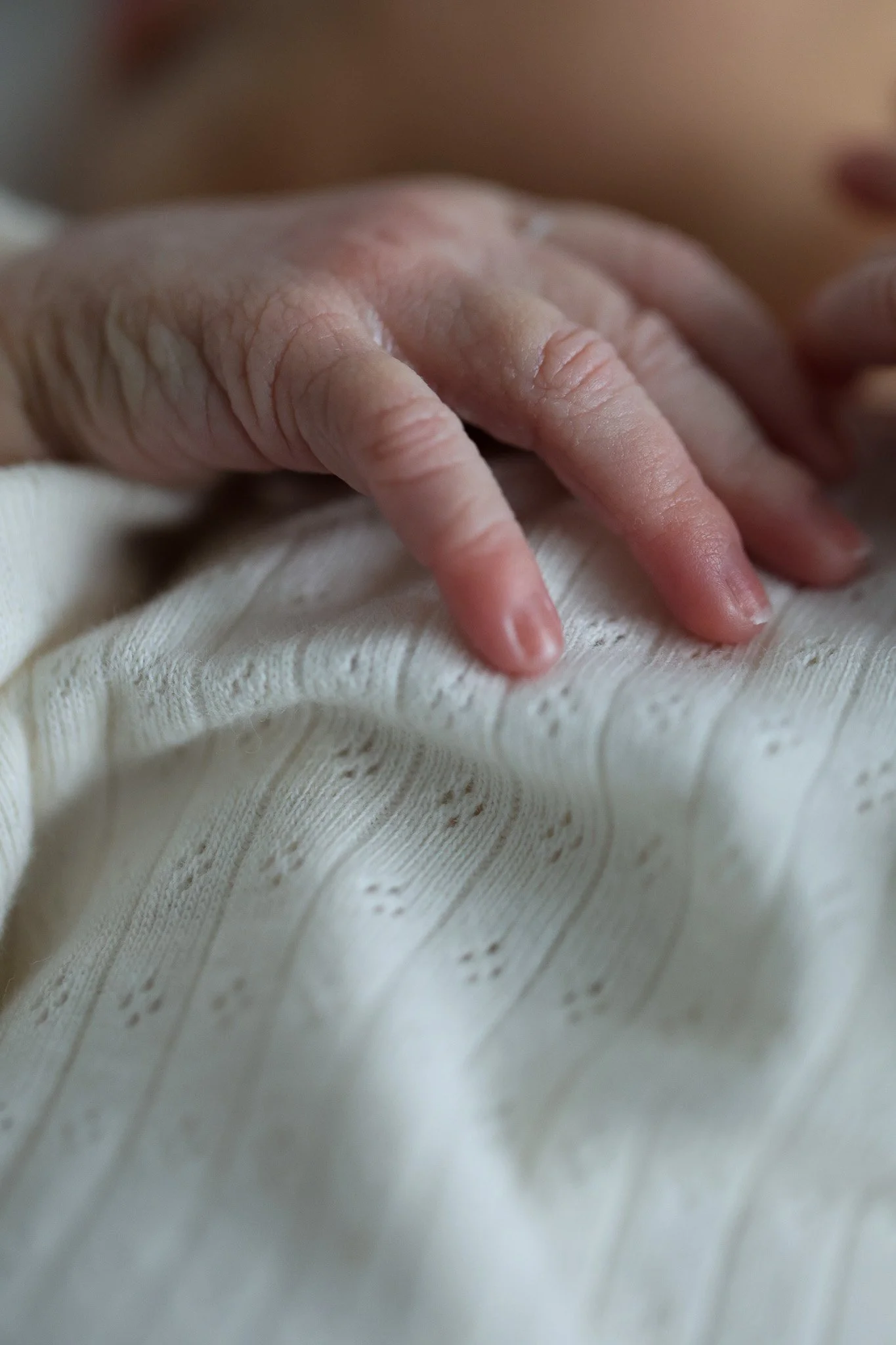 Close-up of a baby's hand resting on light-colored fabric.