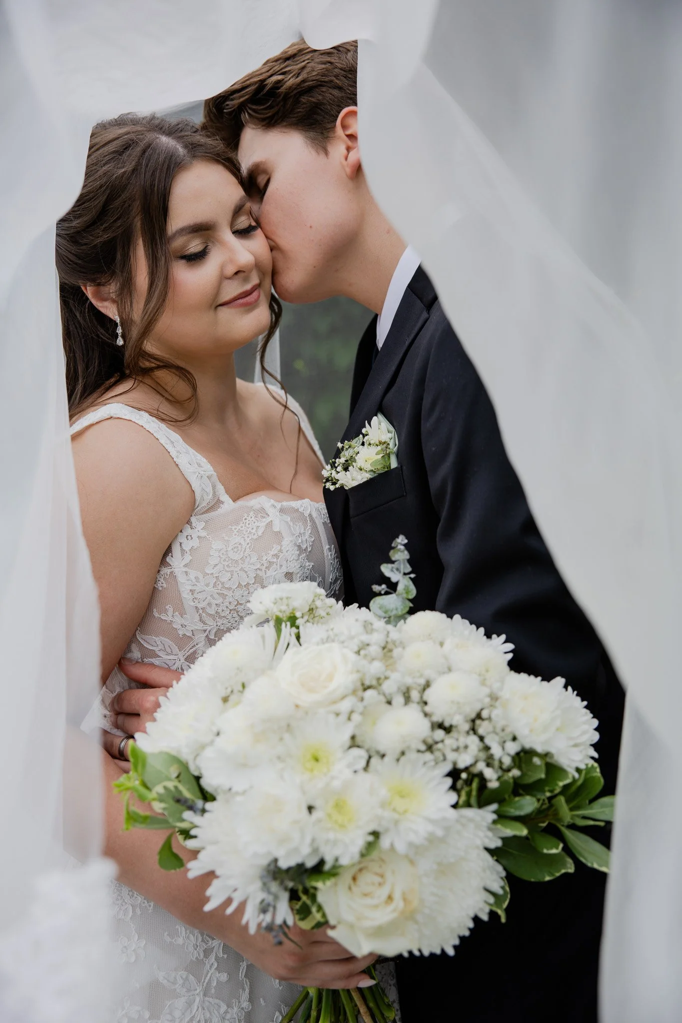 A bride and groom sharing a moment during their wedding, with the bride holding a large bouquet of white flowers.