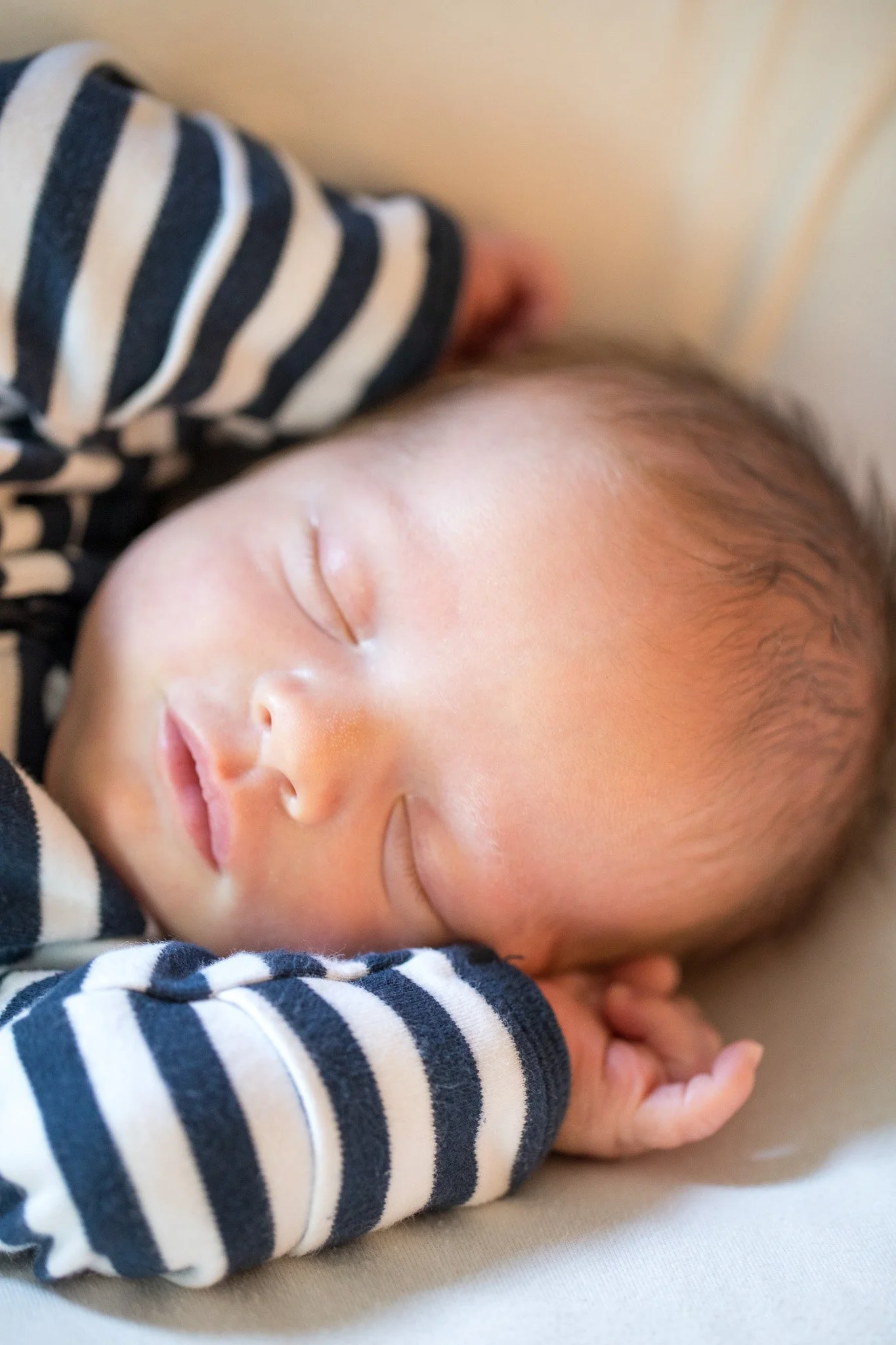 Close-up of a sleeping baby with hands near face, wearing a black and white striped shirt.