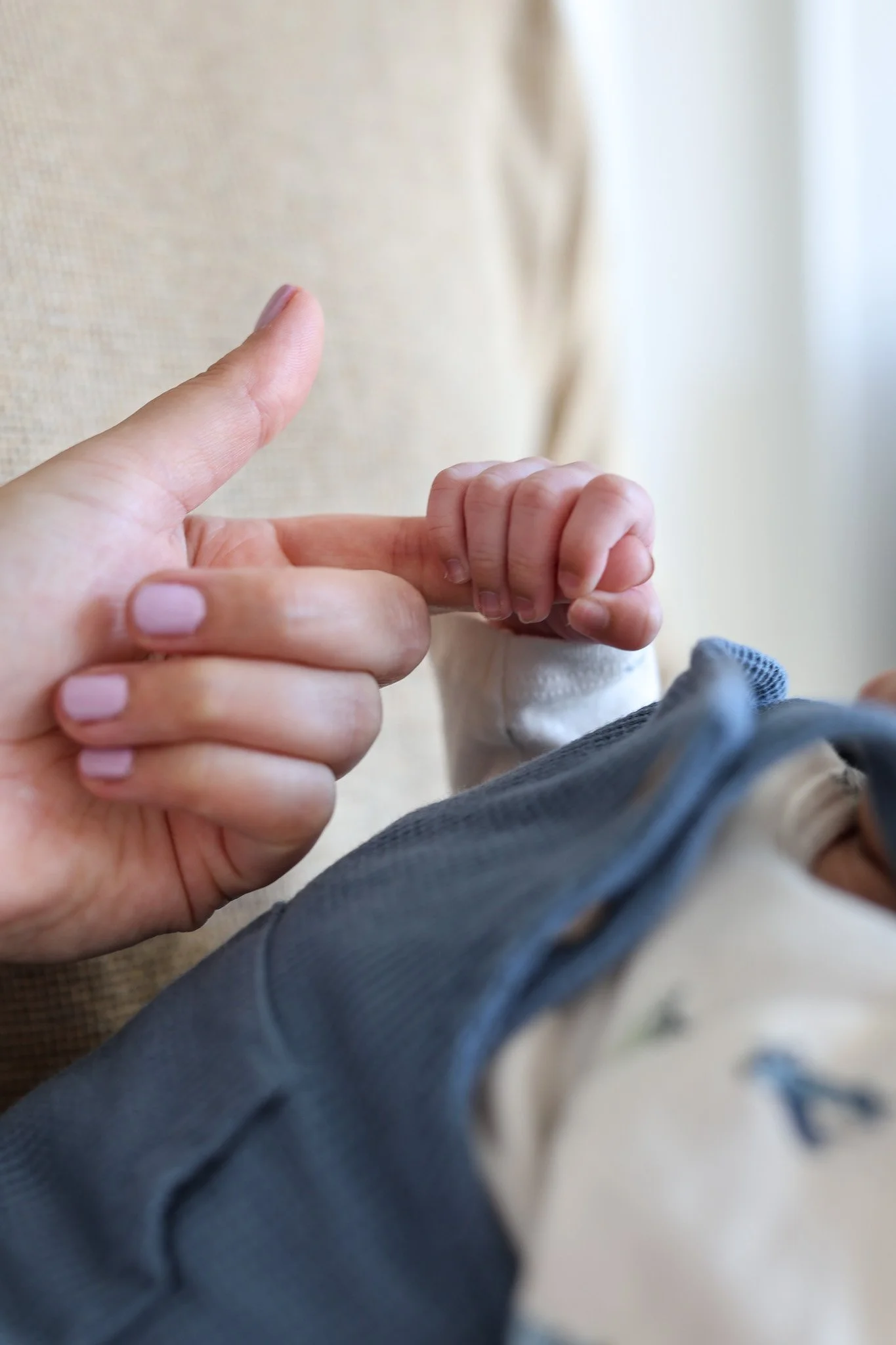 Close-up of an adult holding a baby's hand, both hands visible with a blurred background.