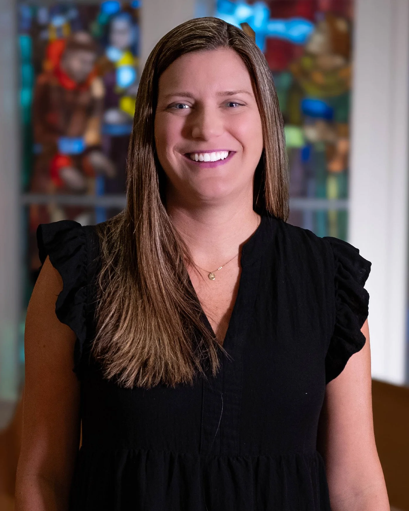 A woman with brown hair in a black dress smiling in front of a colorful background.