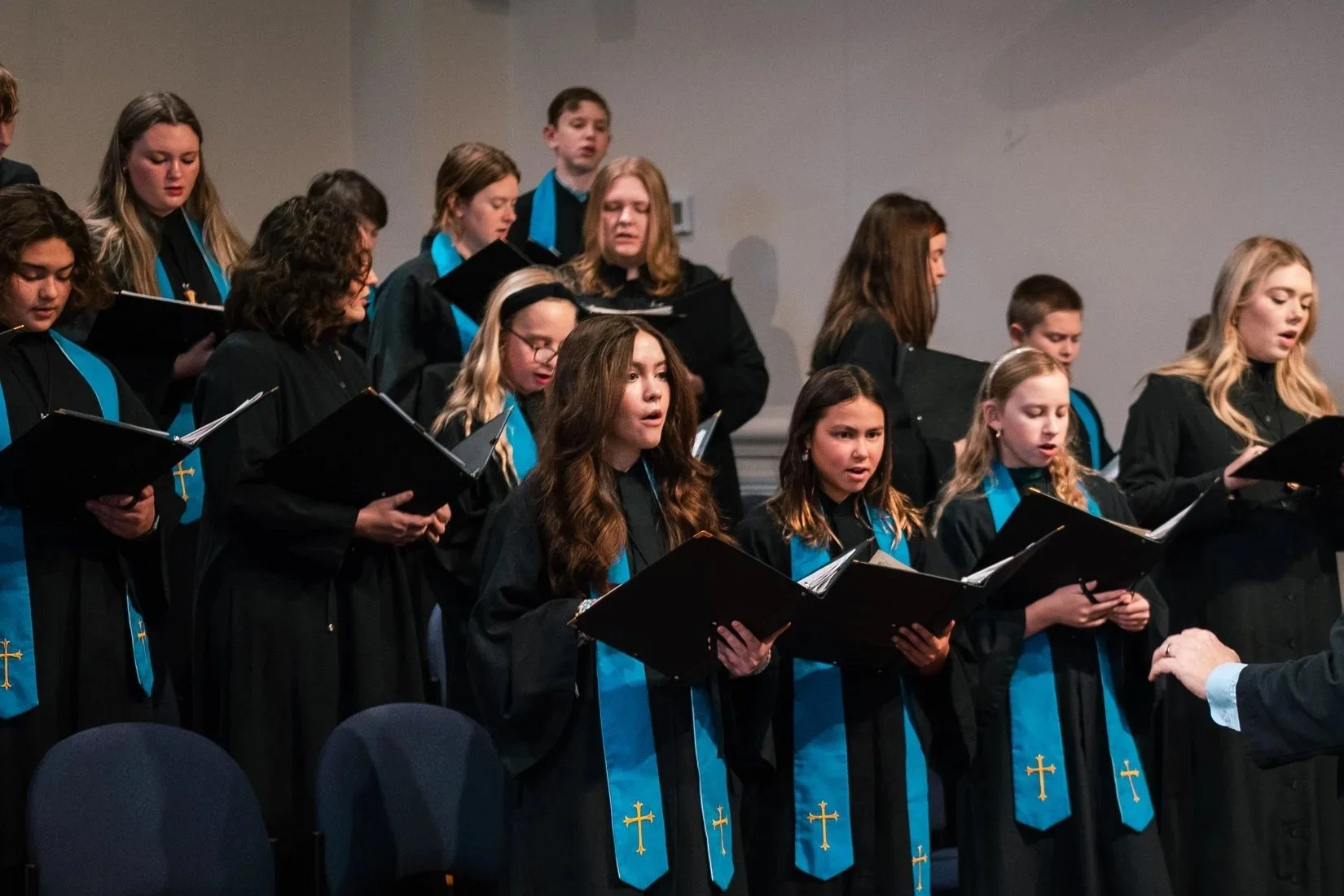 A choir performing on stage with a conductor, with a pianist at a grand piano in the foreground, during a holiday or Christmas event.