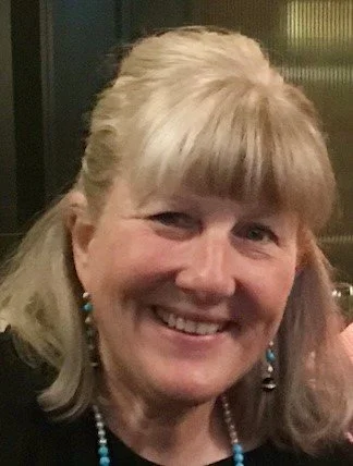 Close-up of a smiling woman with blonde hair, wearing turquoise earrings and a beaded necklace.