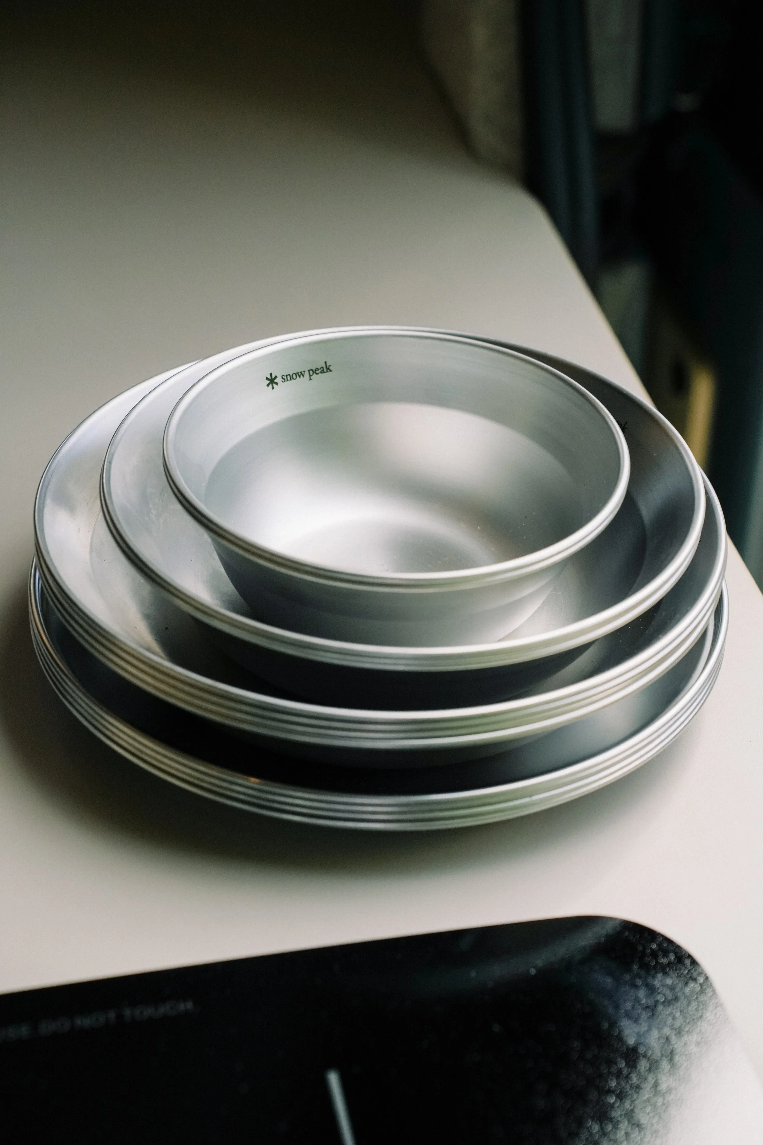 Stack of Snow Peak aluminum bowls and plates on a white surface.