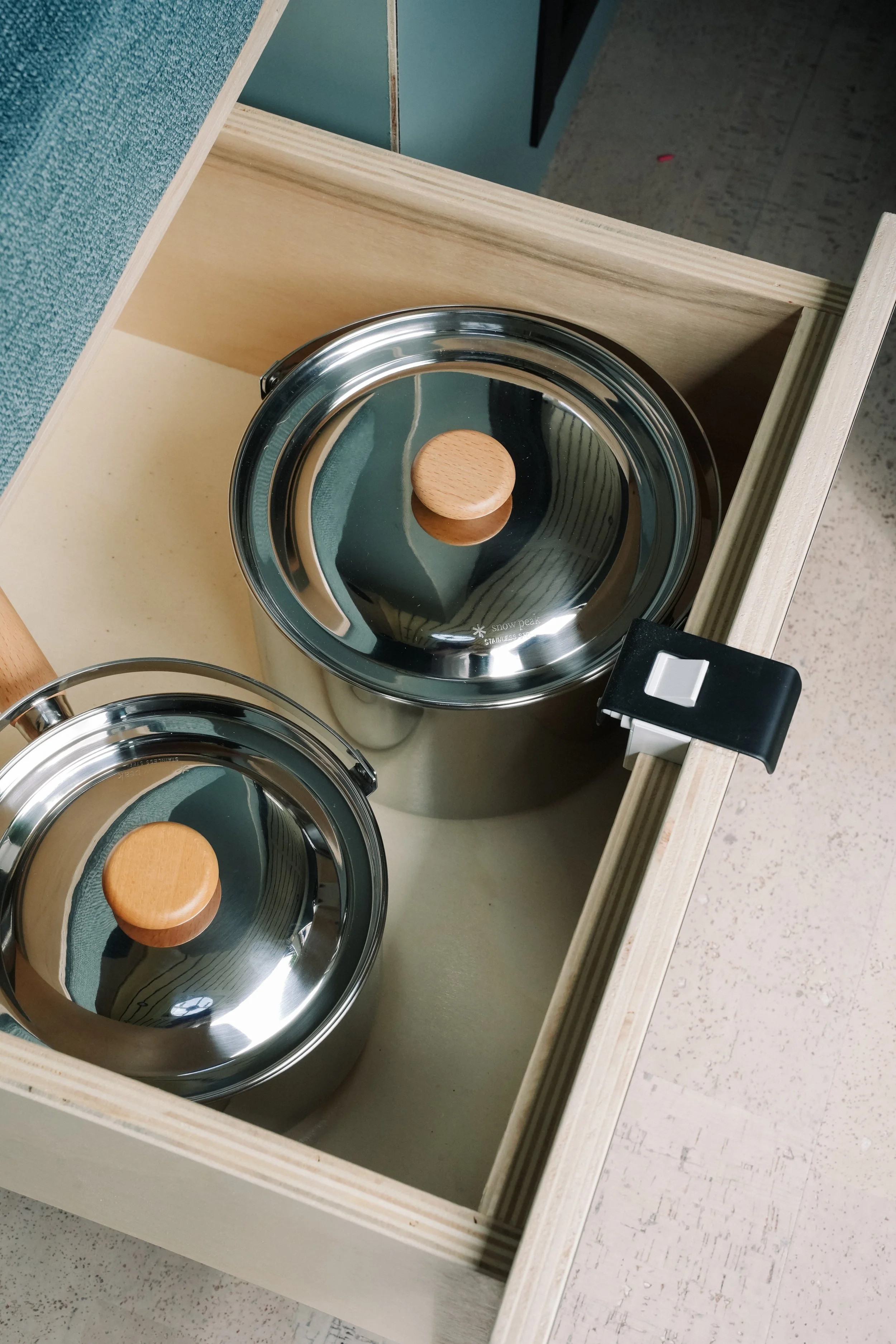 Two stainless steel pots with wooden lids inside a wooden drawer.