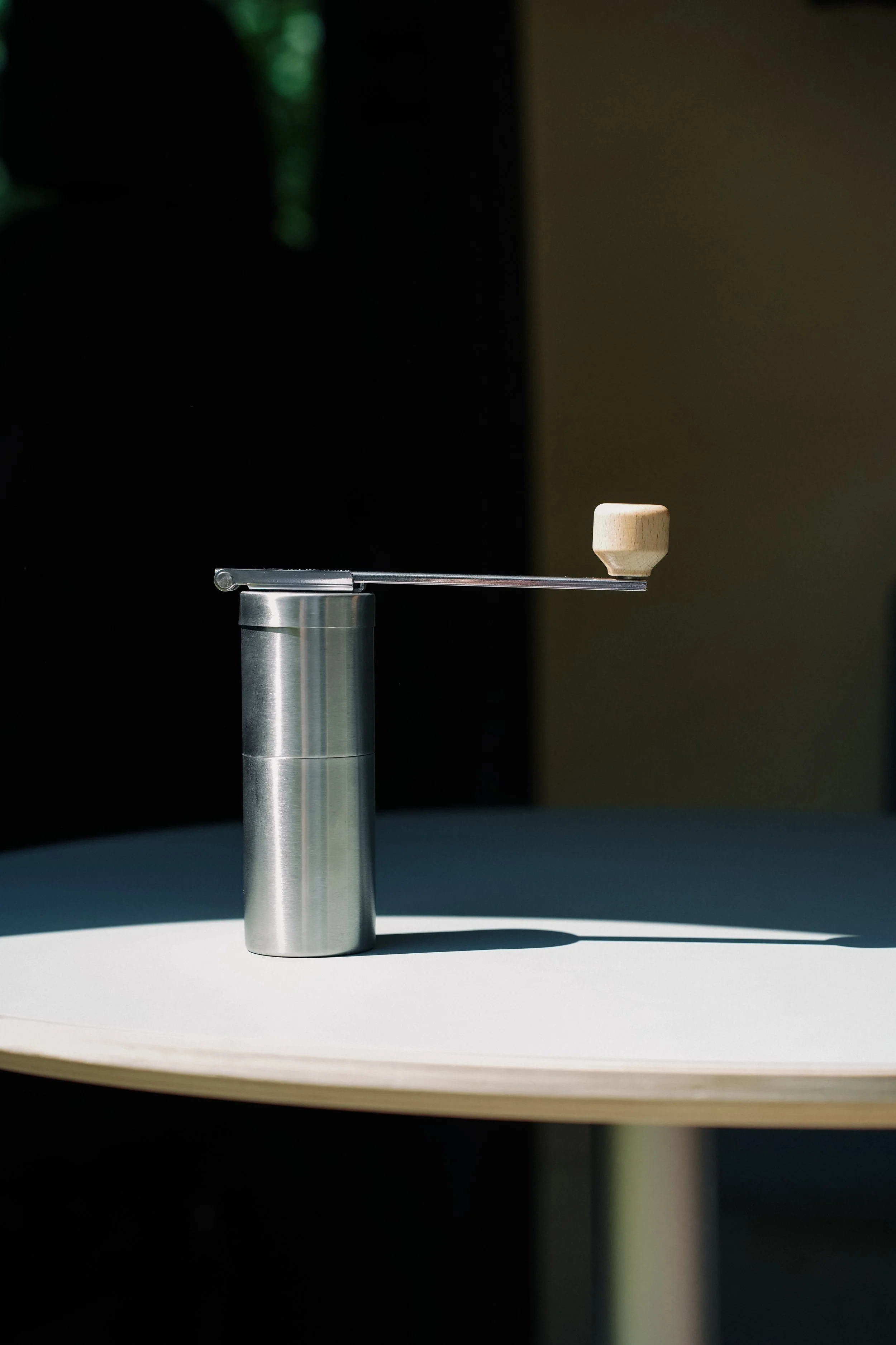 A metal balancing scale with a wooden weight on one side, placed on a white surface, casting a shadow, with a dark background and natural light.