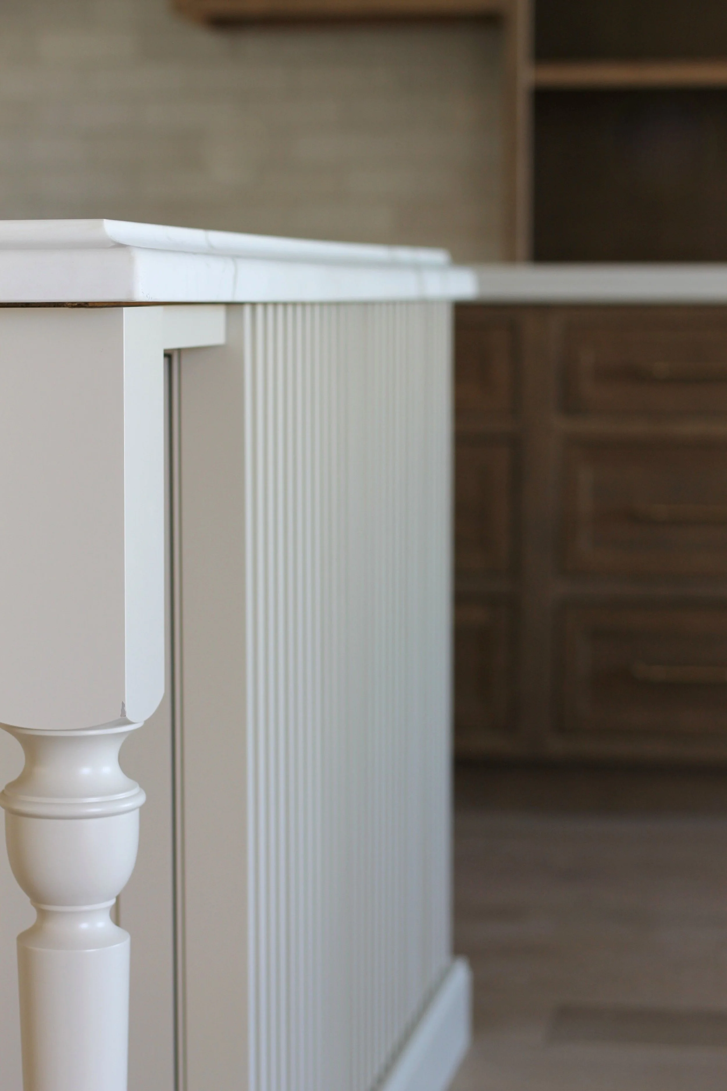 Close-up of a white kitchen island with a decorative leg in a modern kitchen.