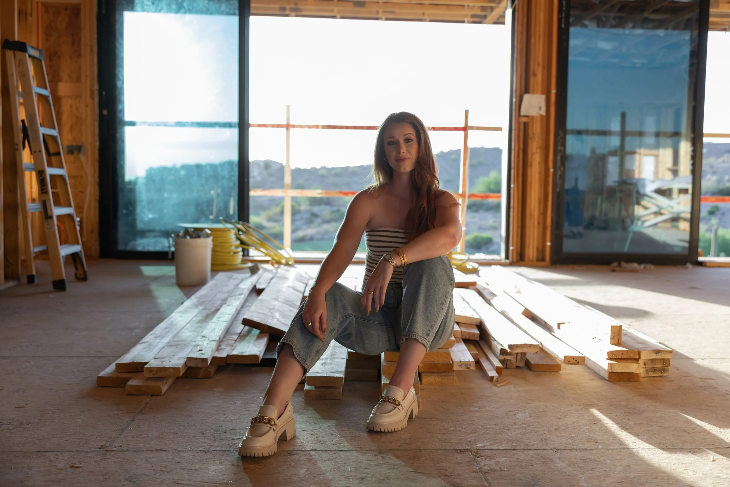 Interior designer Alyssa Warring seated inside framed custom home under construction, highlighting collaborative design-build process with Wren House Design in Arizona.