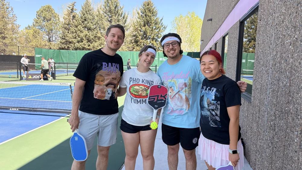 Four players with paddles beside the outdoor courts.