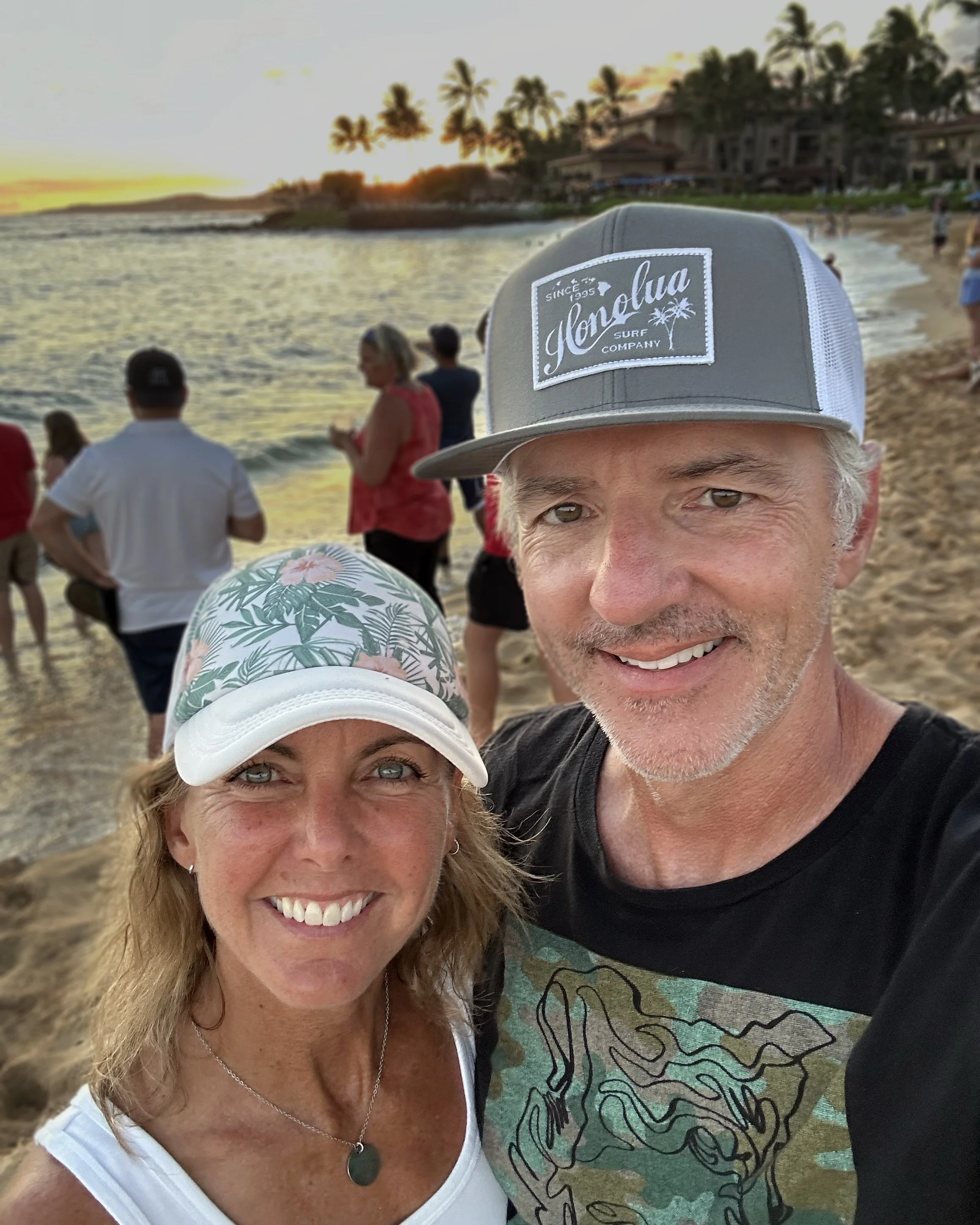Couple taking a selfie on a beach at sunset with palm trees in the background.