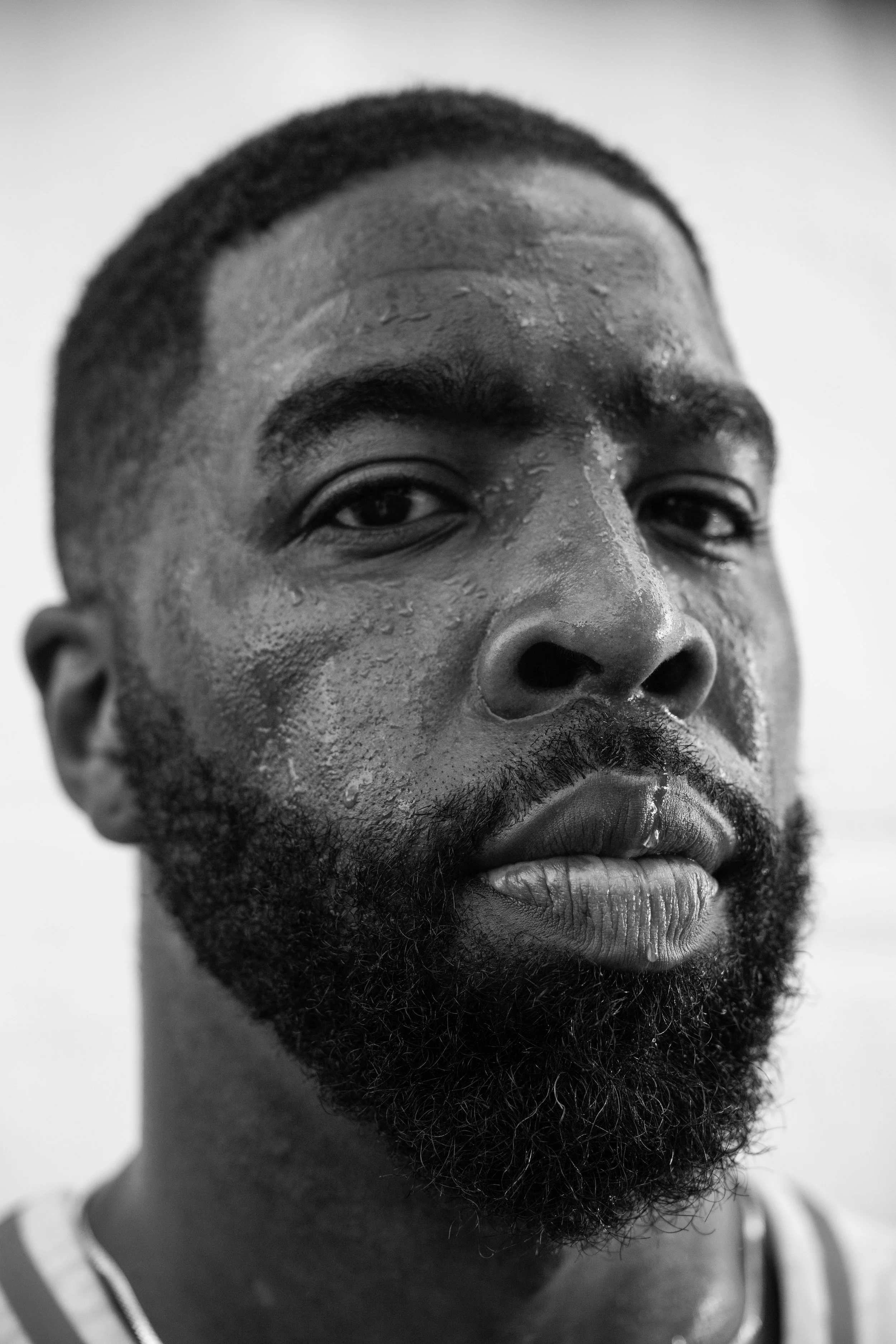 A close-up black and white portrait of a man with wet skin, short hair, and a full beard.
