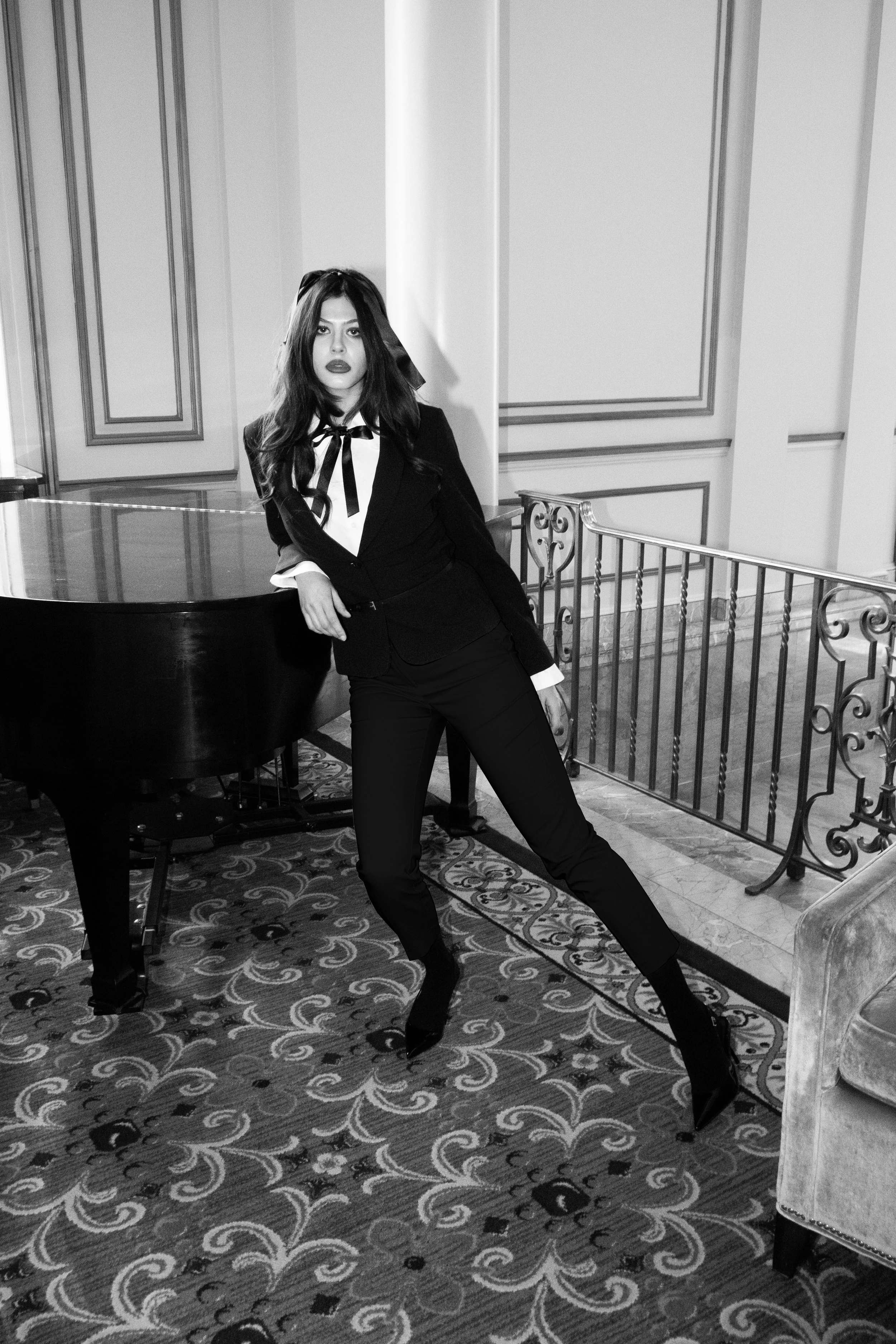 Vancouver BC professional headshot photography. Black and white photo of a woman in a suit leaning against a grand piano in an elegant room with patterned carpet and ornate railings.