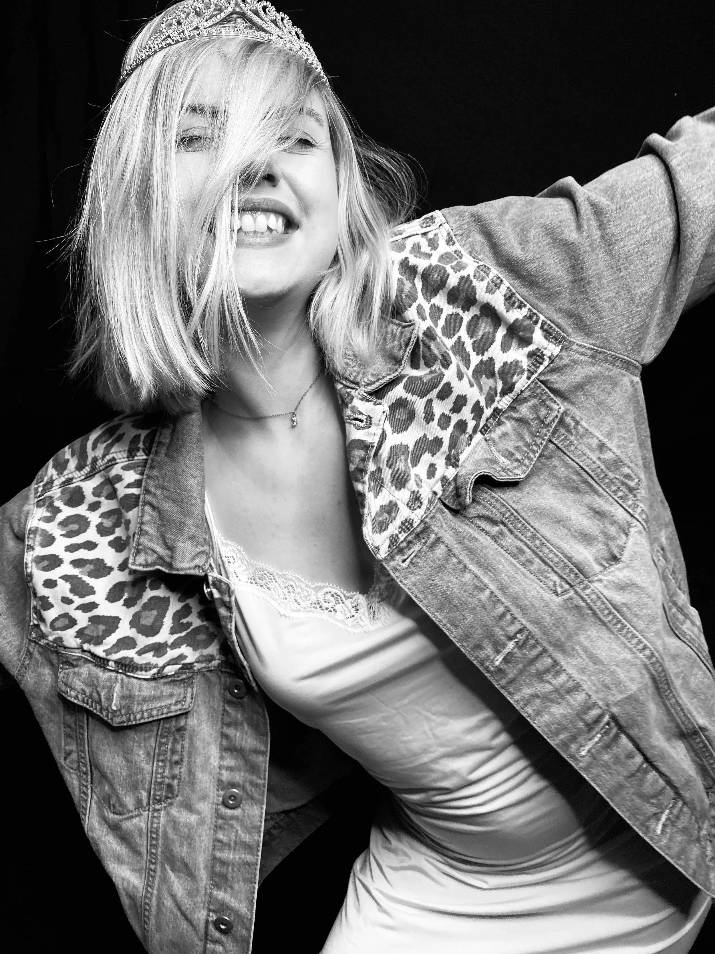 Vancouver BC professional headshot photography. Black and white photo of a woman wearing a crown and a denim jacket with leopard print accents, smiling and posing with her arm extended outward.