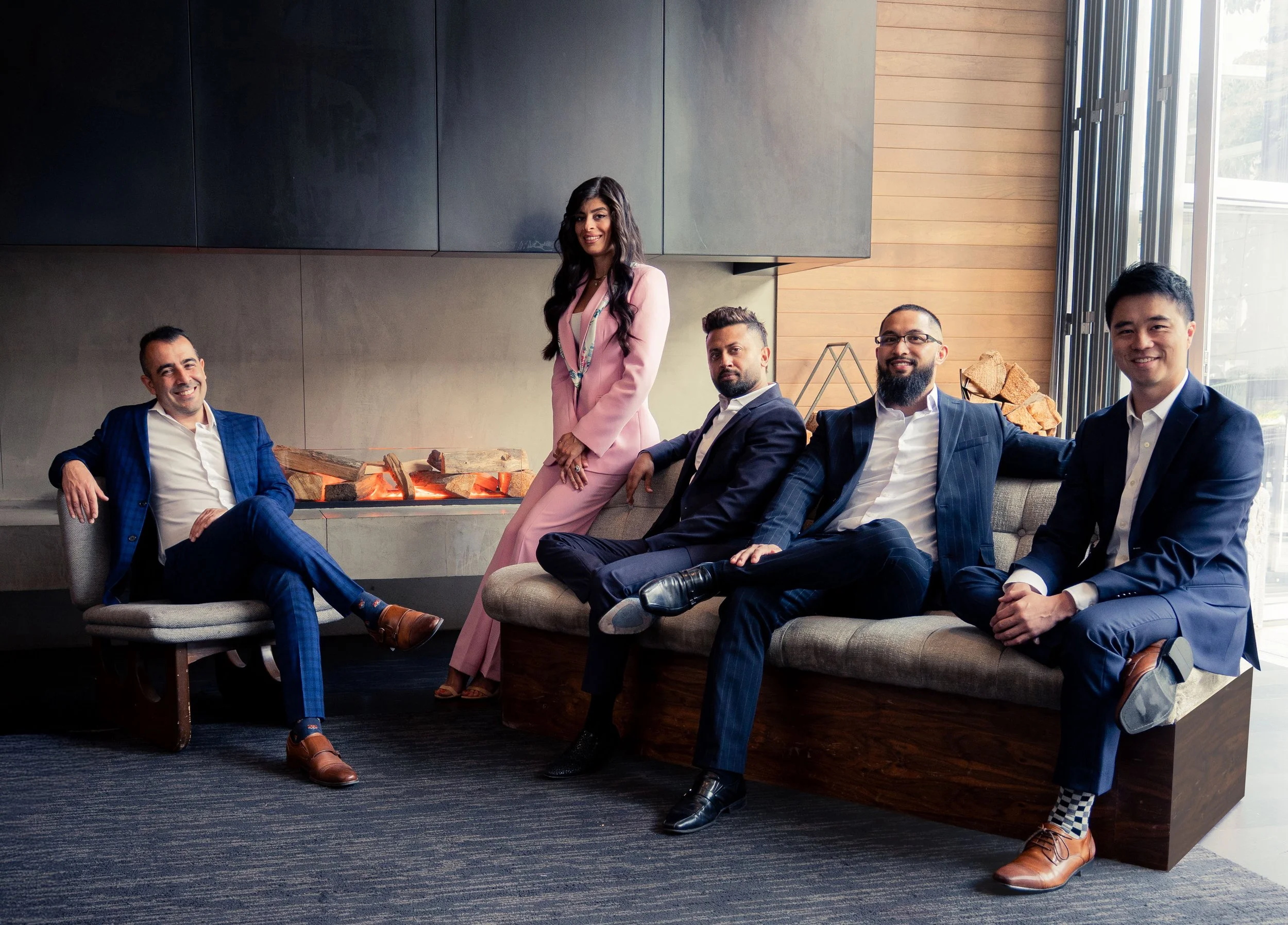 Vancouver BC professional headshot photography. Five diverse professionals in business attire posing in a modern office lounge with a fireplace and large windows.