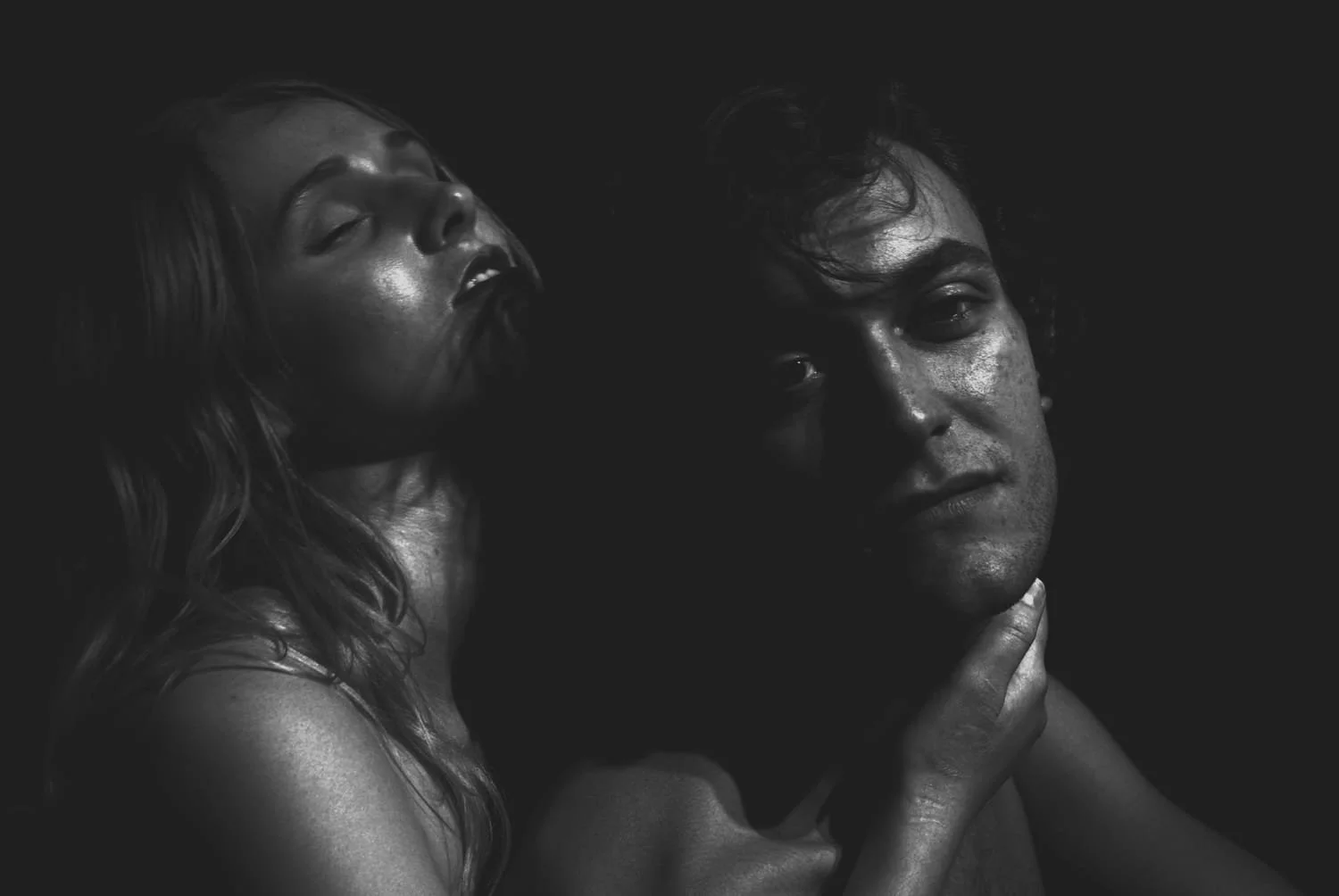 Vancouver BC professional headshot photography. Black and white photograph of a woman with closed eyes leaning on a man's shoulder, who is looking slightly to the side with a serious expression, against a dark background.
