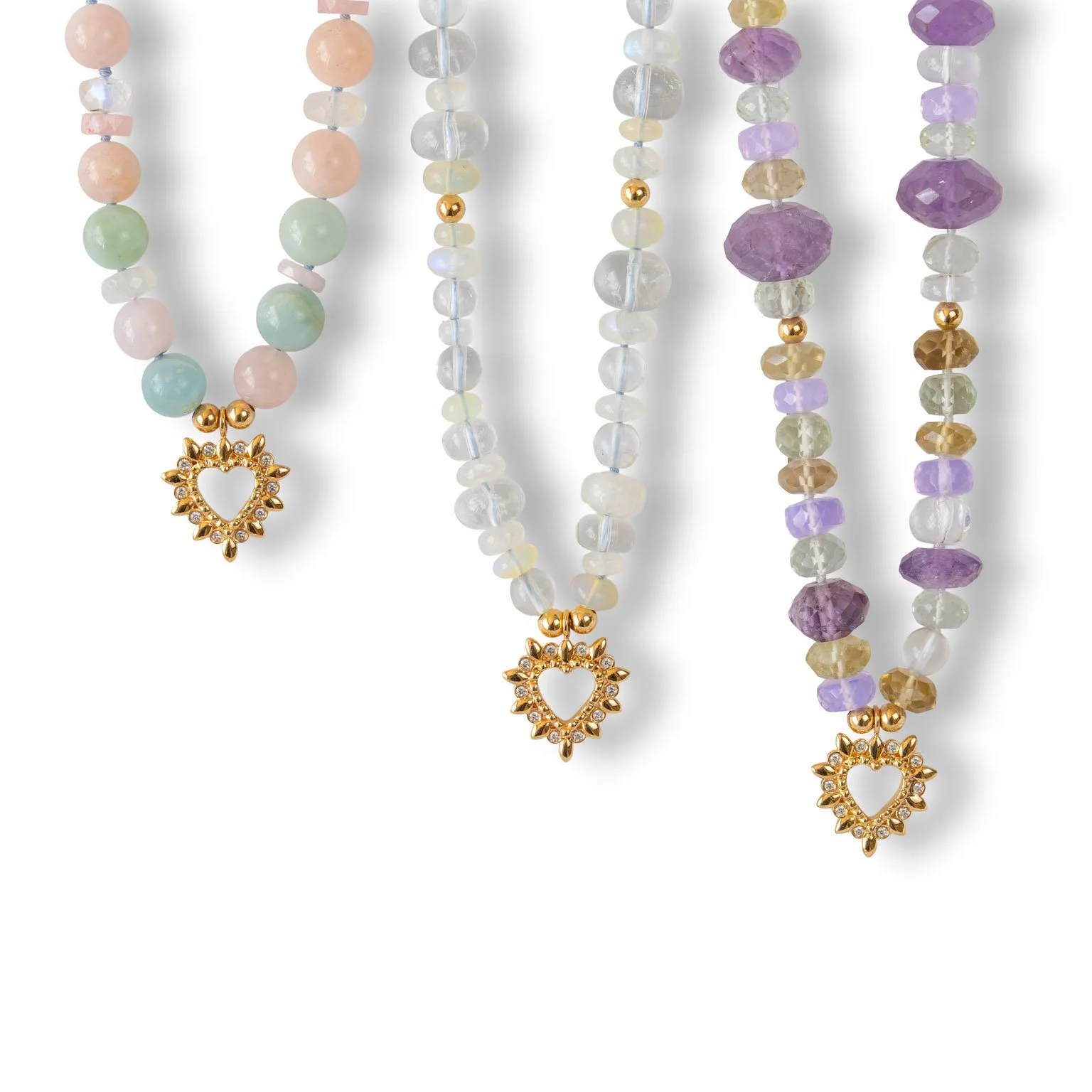 Three beaded necklaces with gold heart-shaped pendants featuring small stones, in pastel and purple hues.