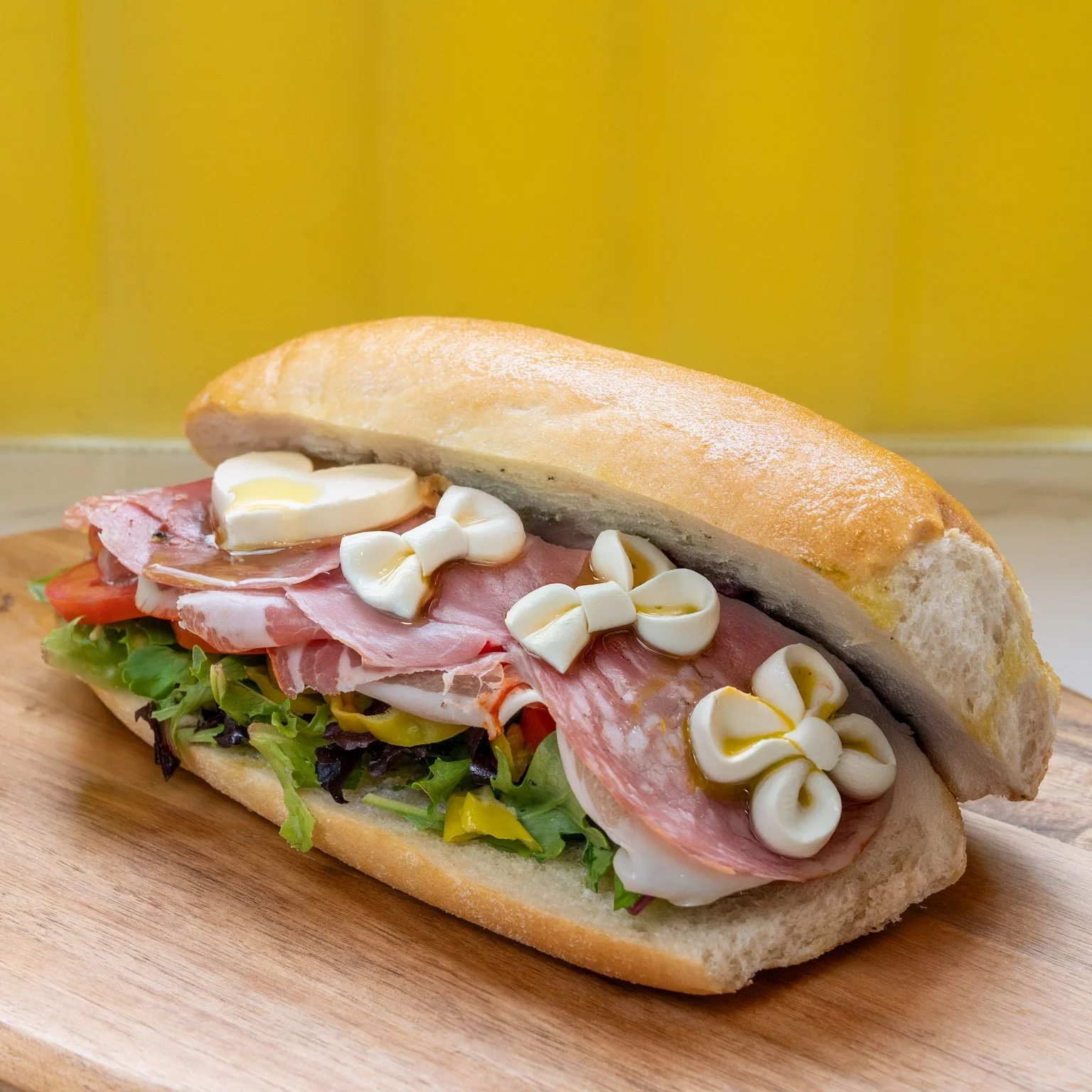 Sandwich with lettuce, tomato, ham, cheese, and mayonnaise in a baguette on a wooden board.