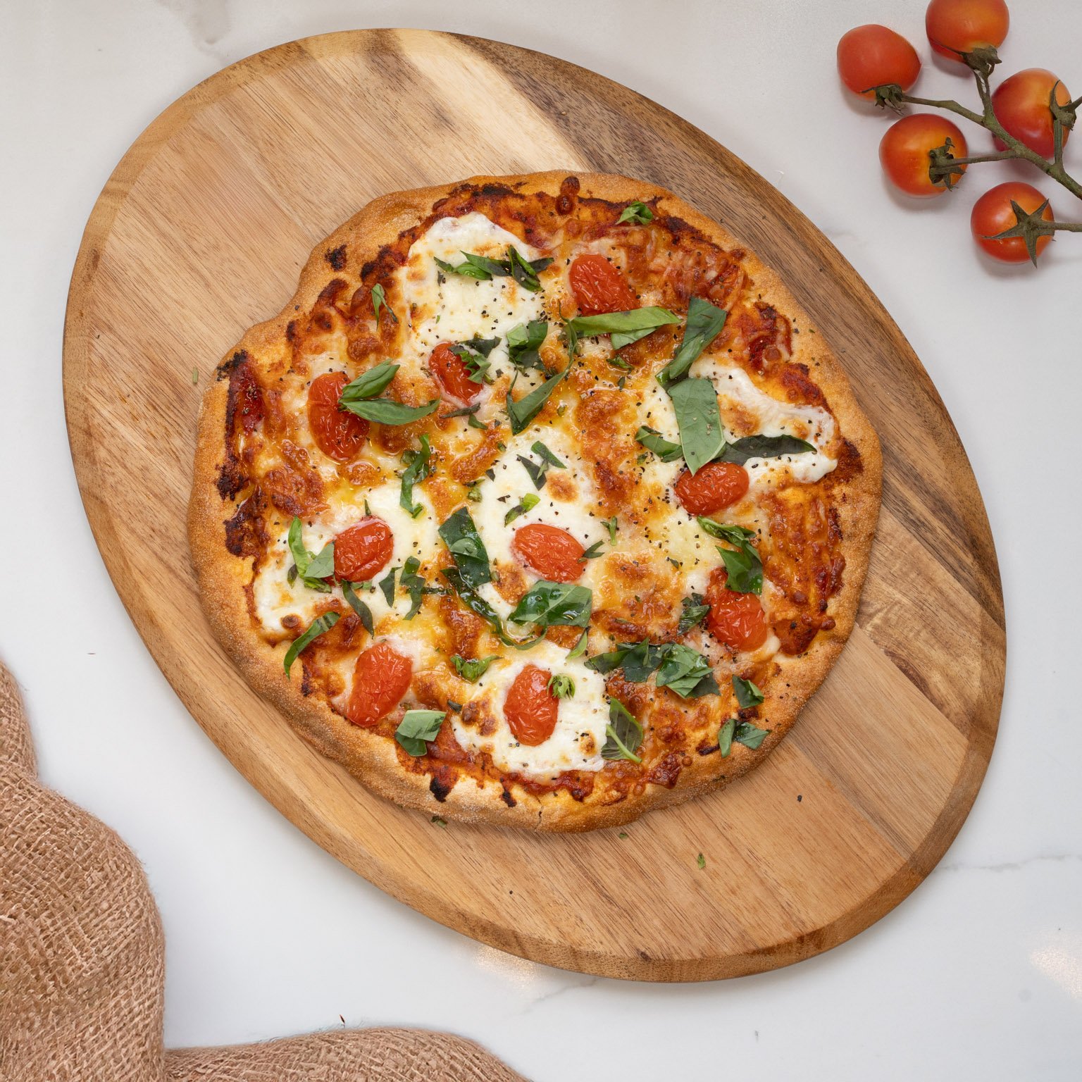 Fresh pizza with cherry tomatoes, melted cheese, and basil leaves on a wooden cutting board.