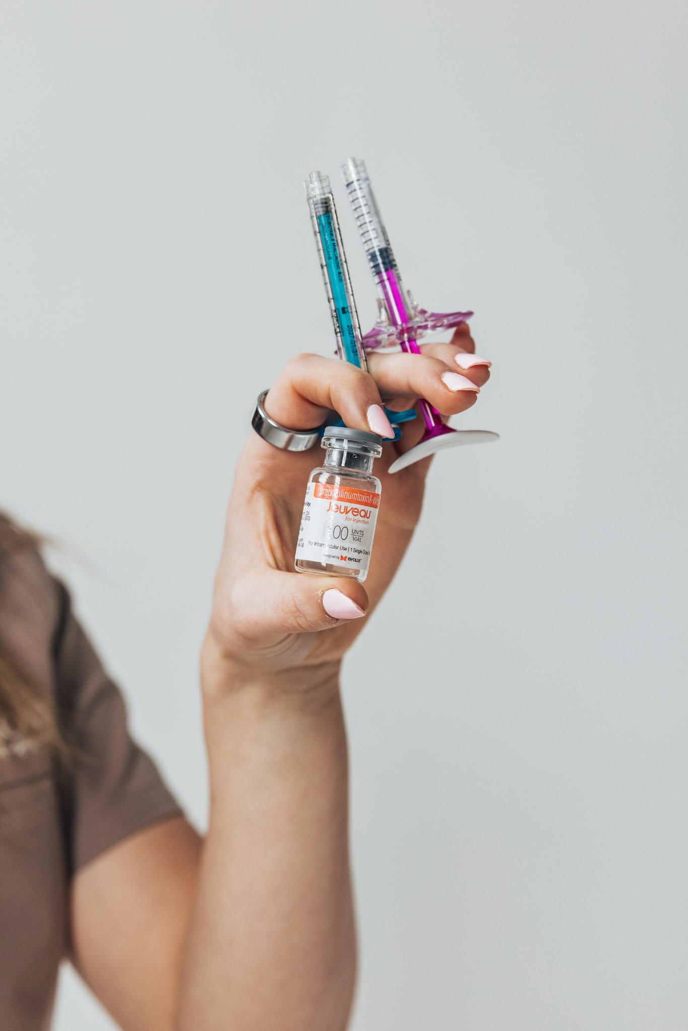 A hand holding a vial of vaccine with a syringe and a medical needle.