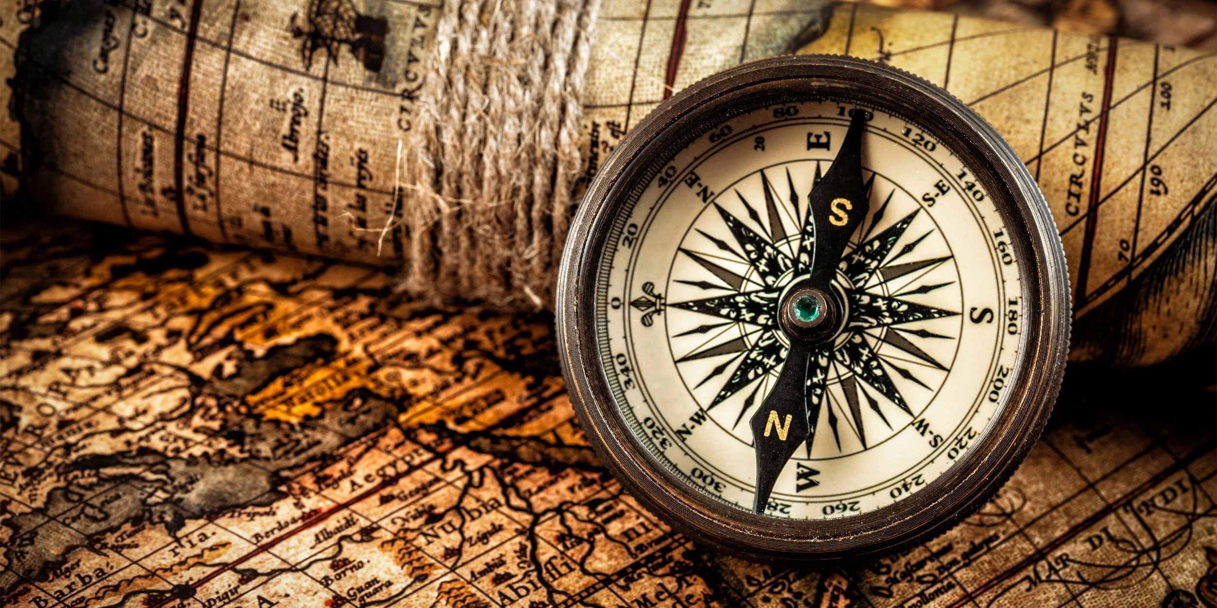 A vintage compass resting on an old scroll map, with part of the map rolled up in the background.